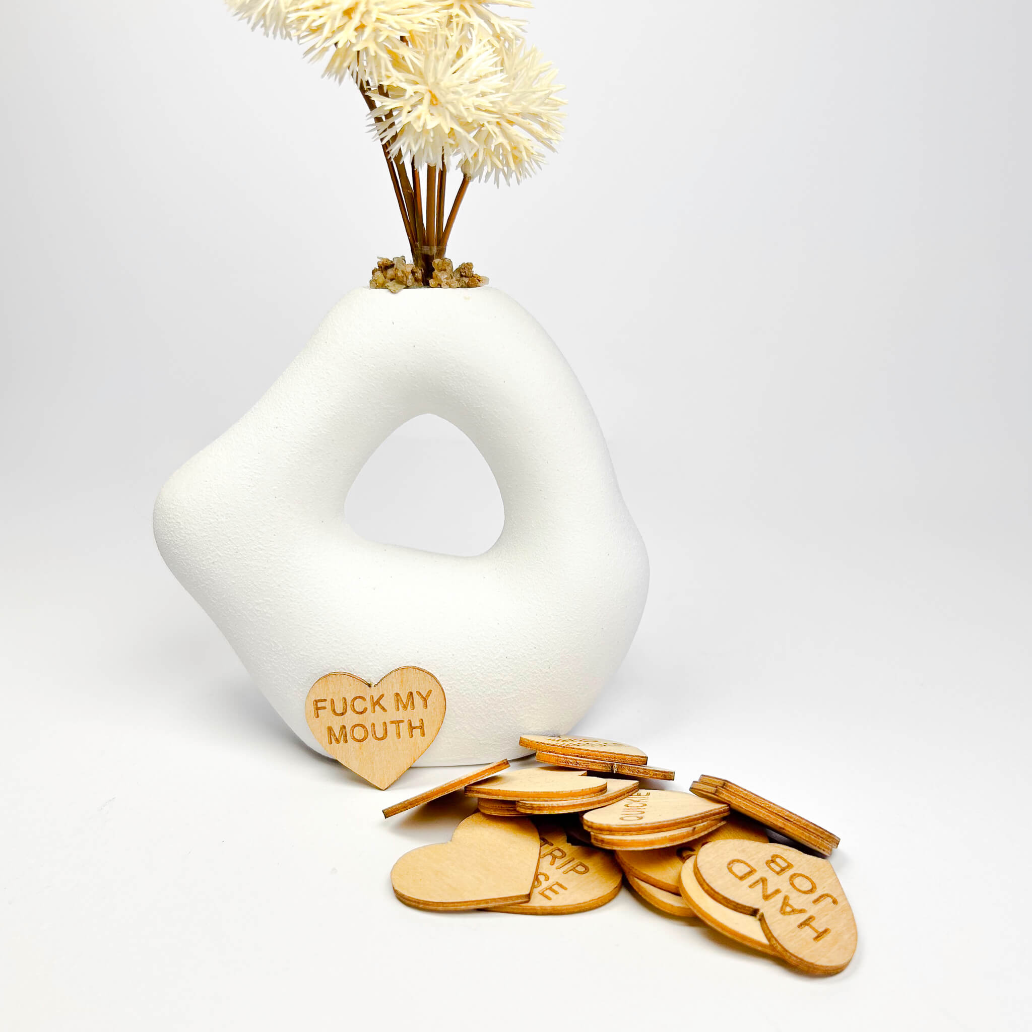 White vase with decorative elements and wooden heart-shaped tokens on a light gray background