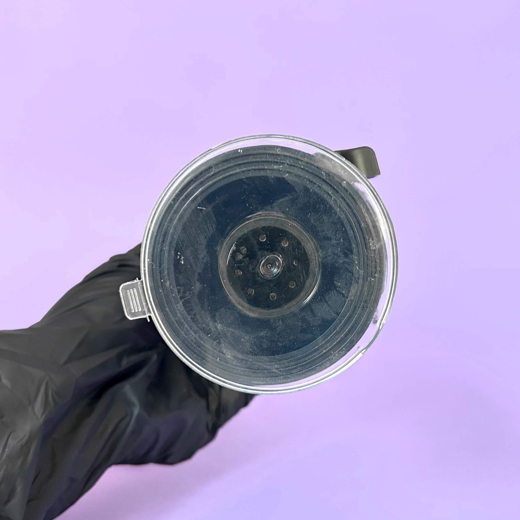 Clear plastic component held by a black gloved hand against a purple background