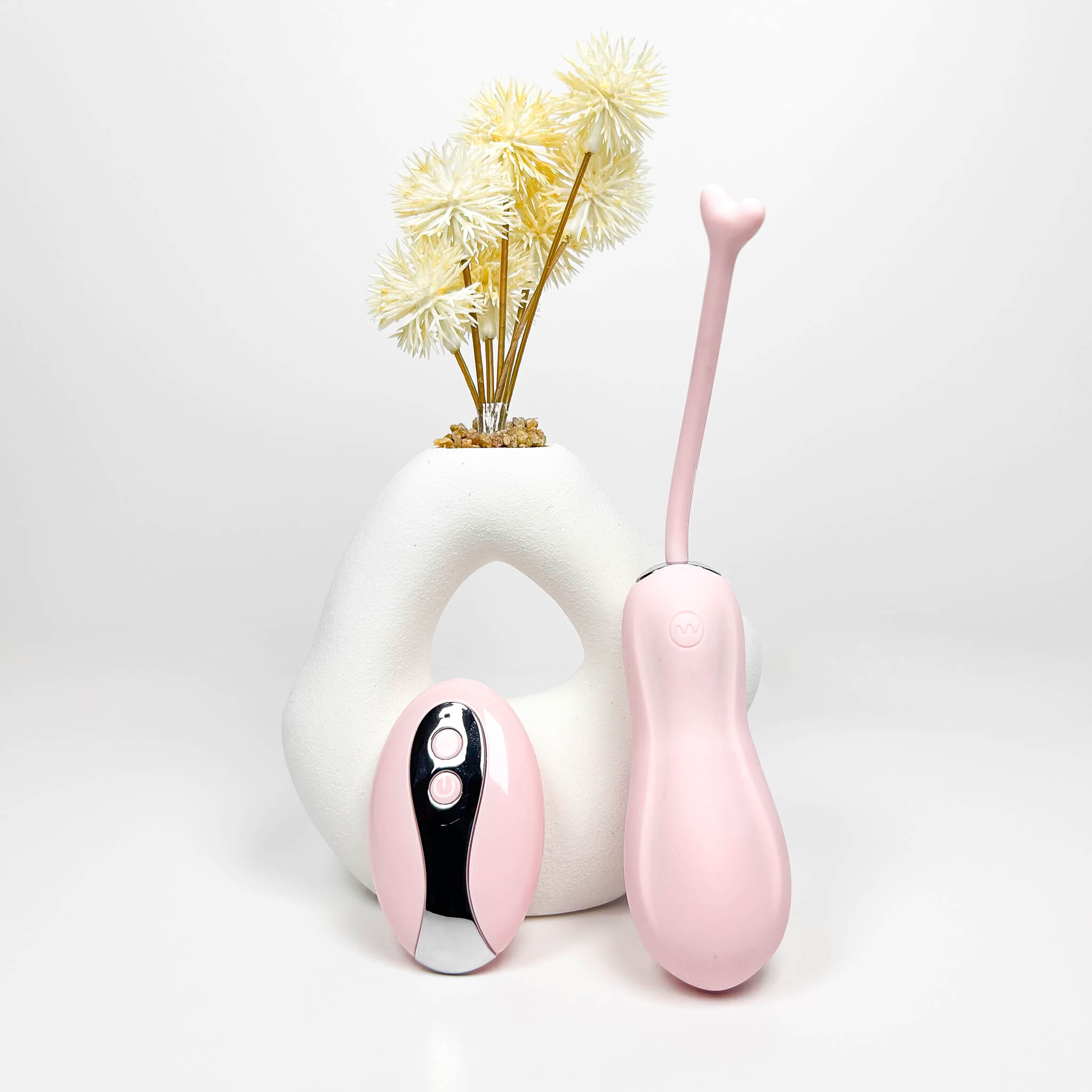 a Pink CurvePlay Insertable Remote Vibrator with a white vase containing yellow flowers on a light gray background
