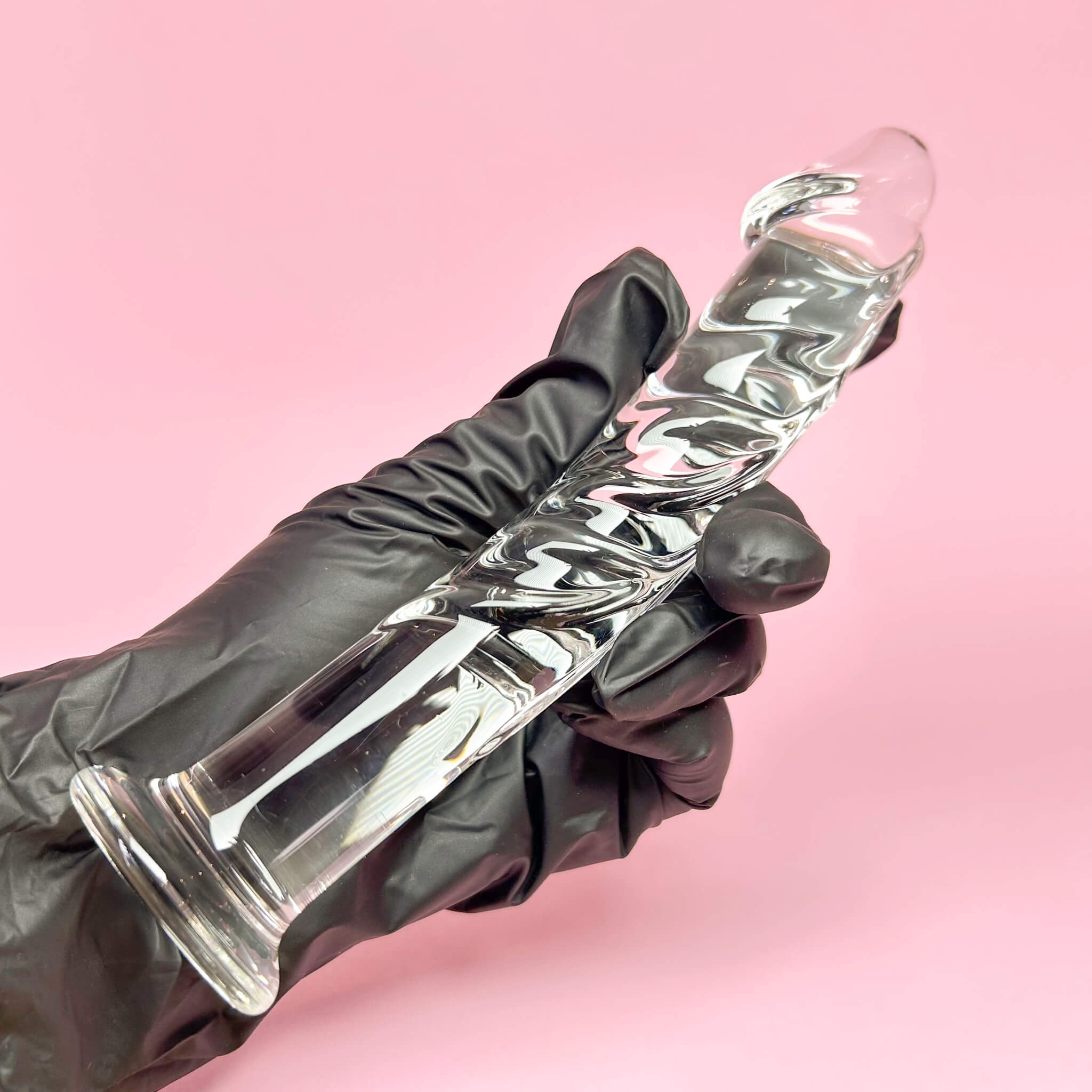 Clear glass curved dildo held by a gloved hand against a pink background