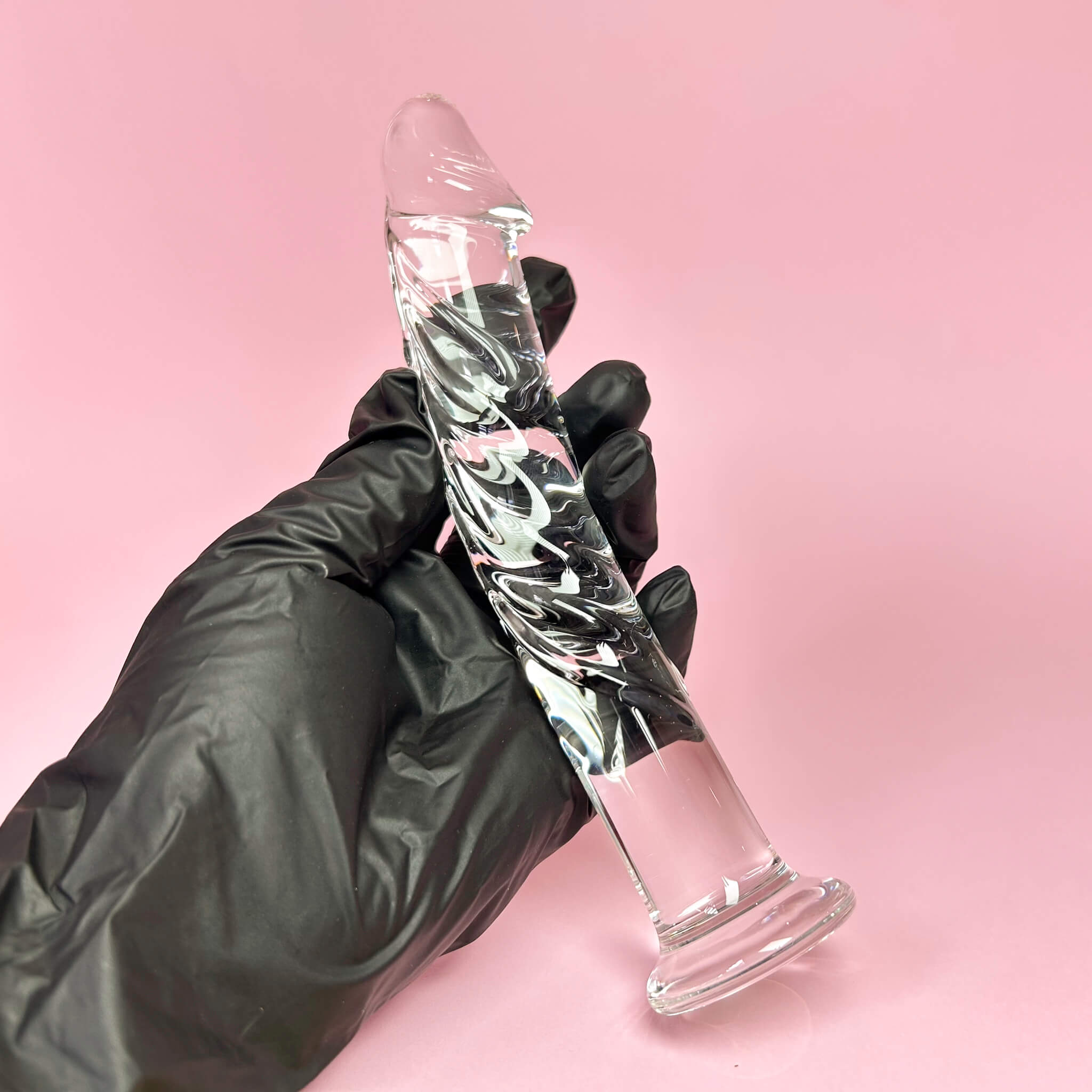 Veiny Glass dildo held by a gloved hand against a pink background