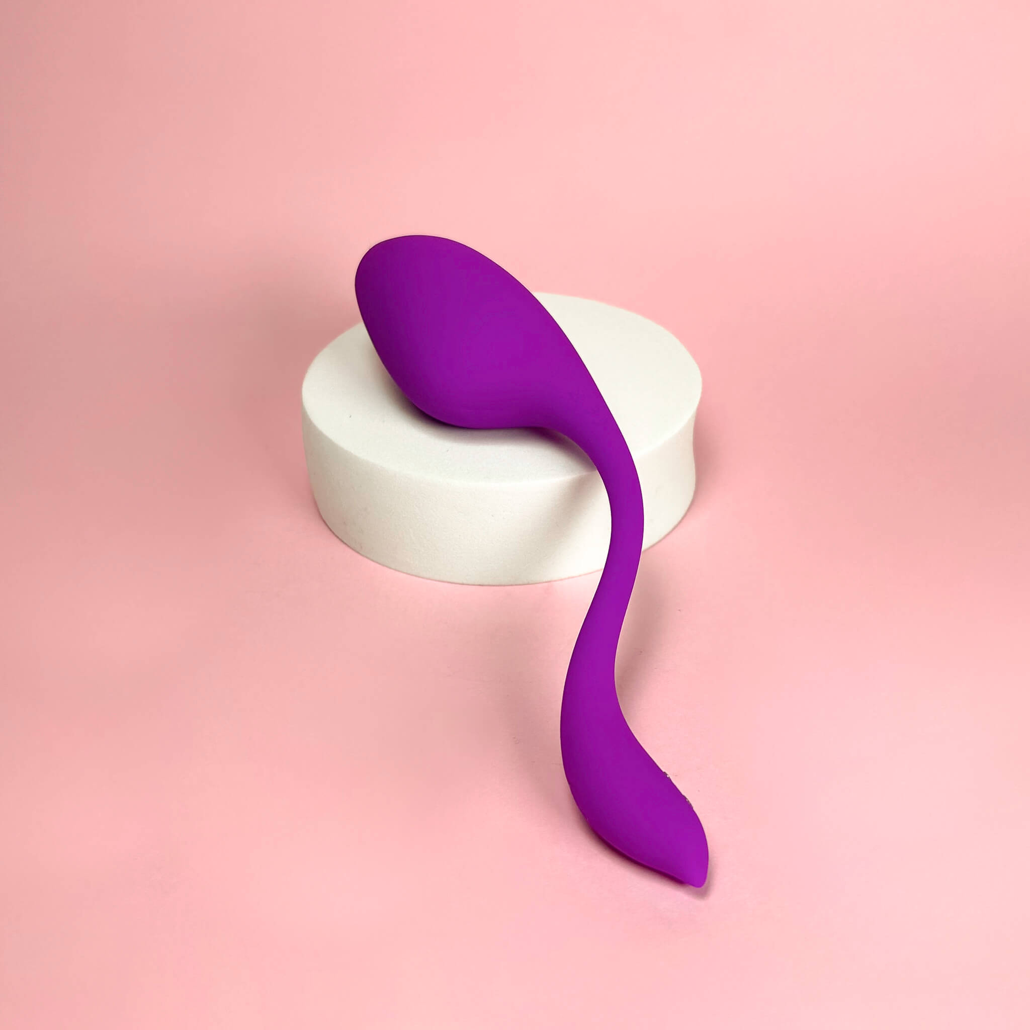 Purple vibrator on a white platform with a pink background