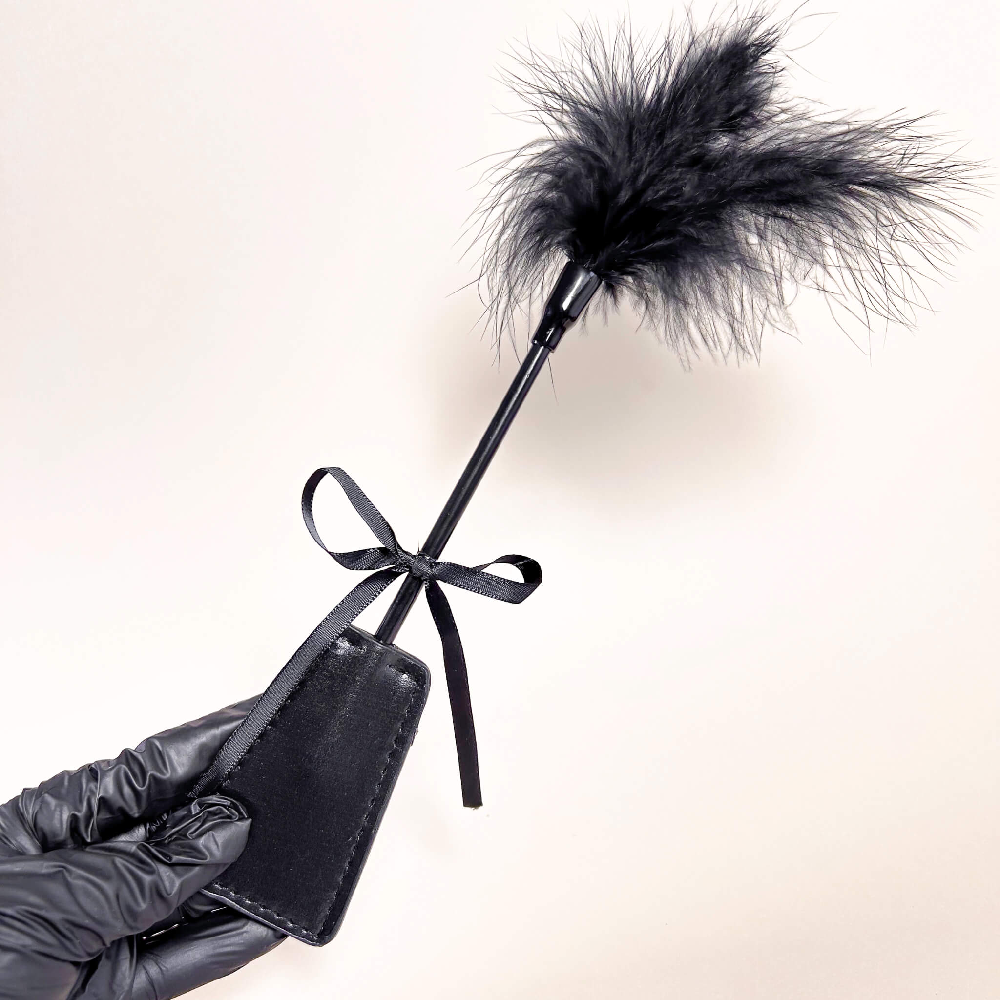 Black leather paddle with feathered end held by a gloved hand on a light background