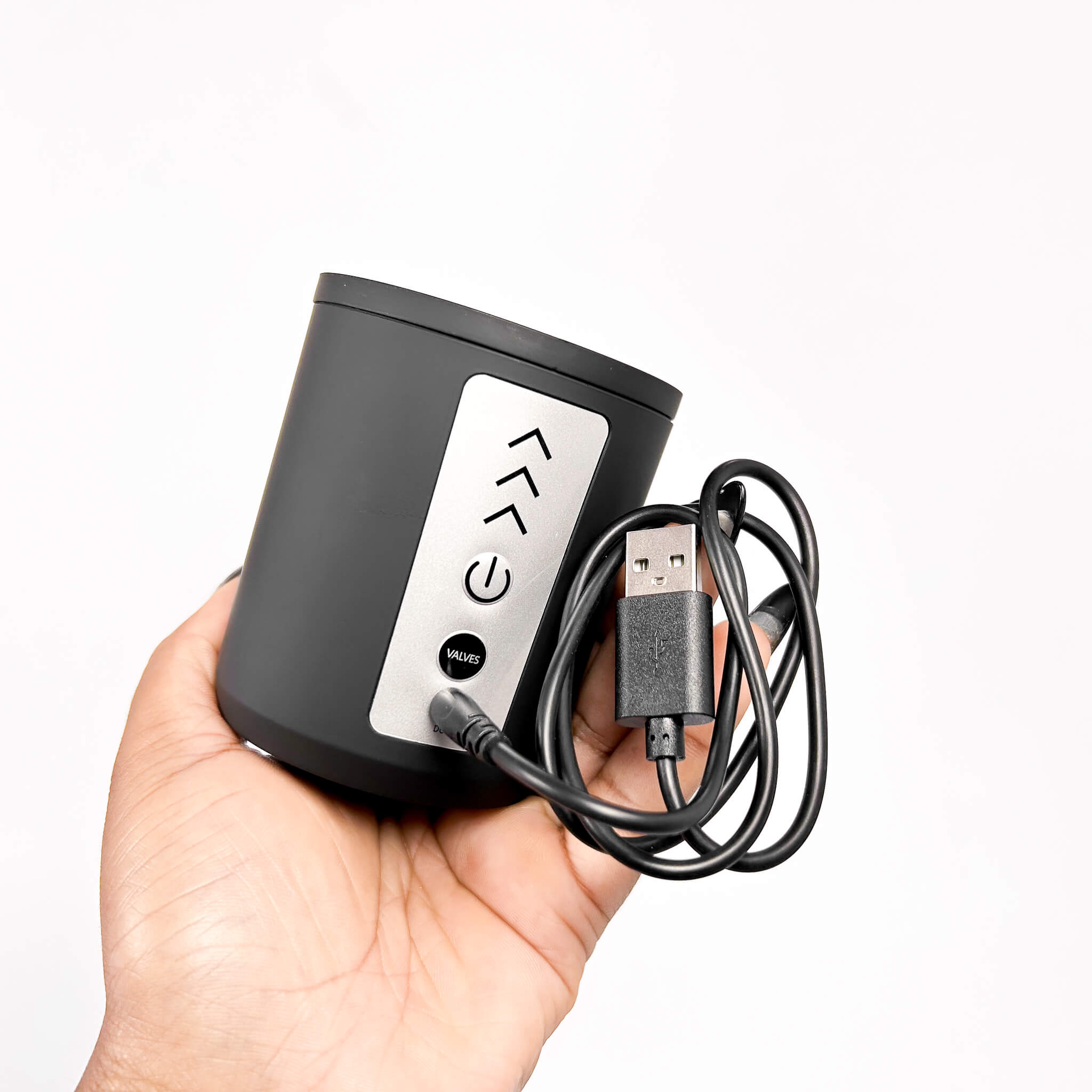 Black electronic device with USB cable held in a hand against a white background