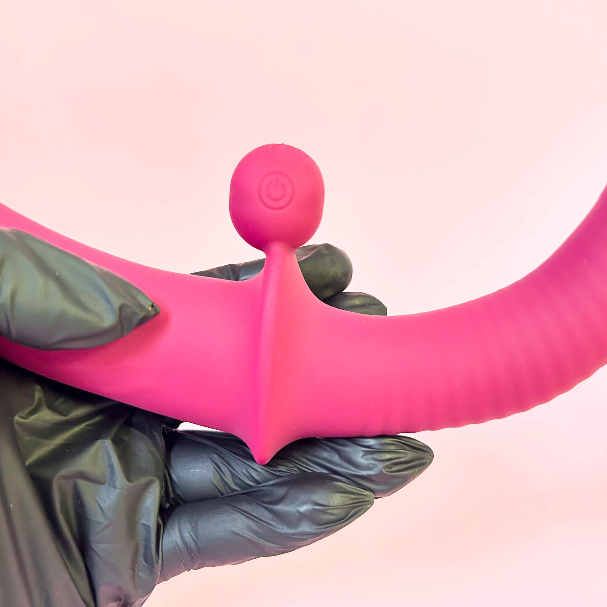Flexible double ended vibrator held by a gloved hand against a pink background