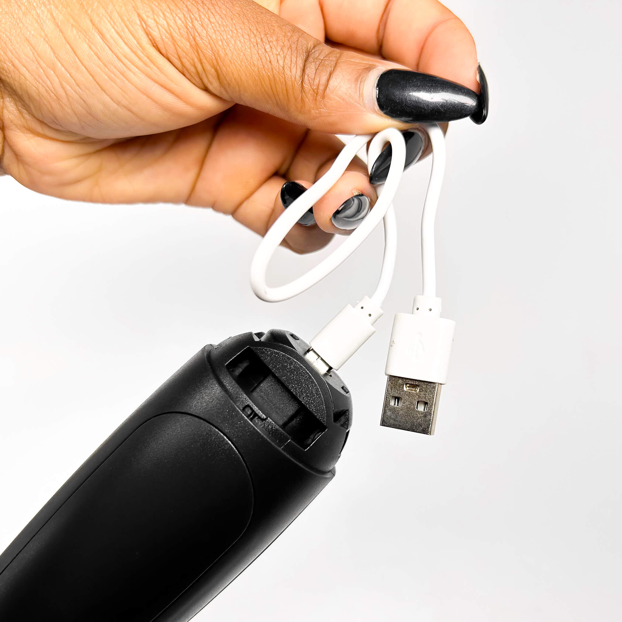 Hand holding a black electronic device with a white USB cable against a white background