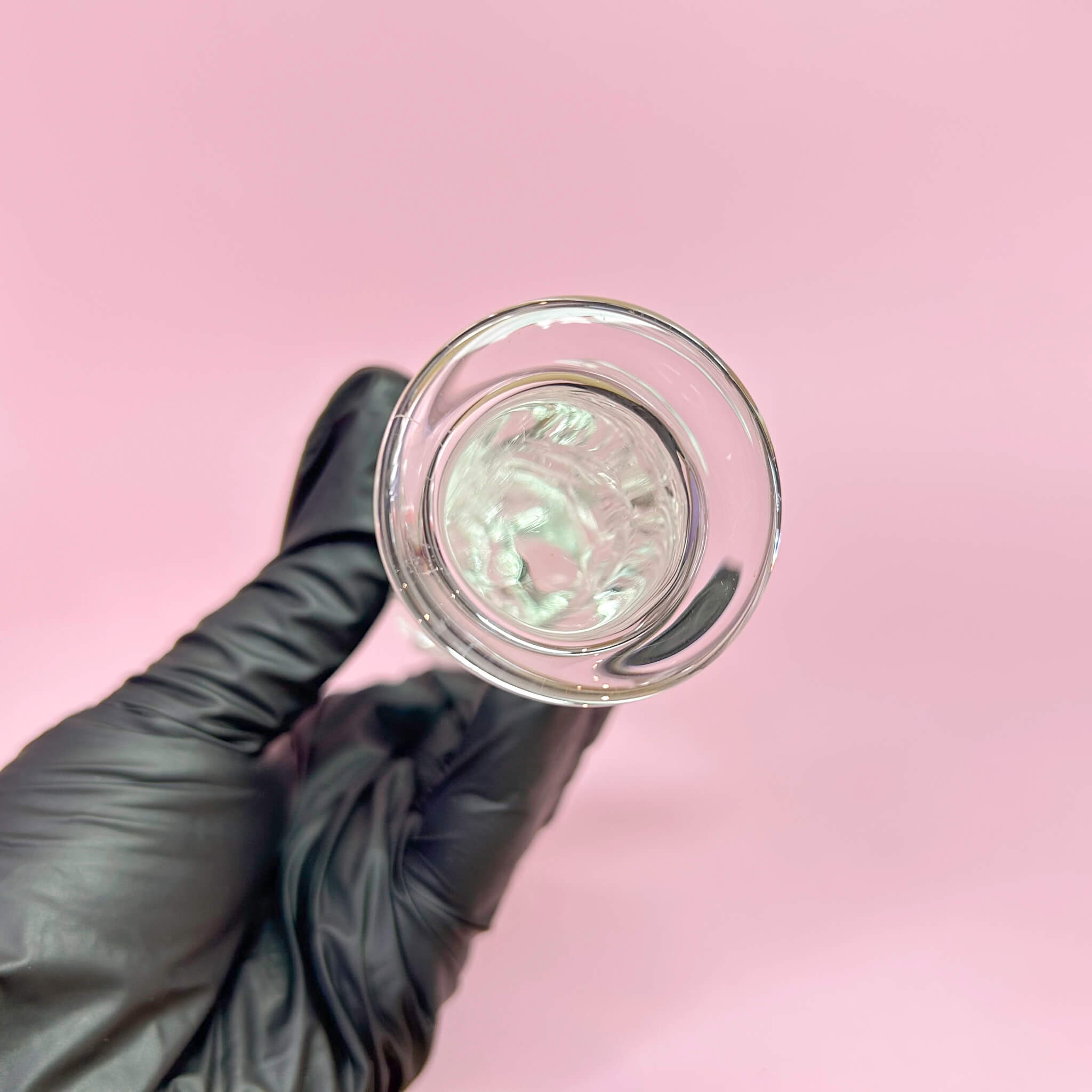 Bottom of glass dildo held by a gloved hand against a pink background
