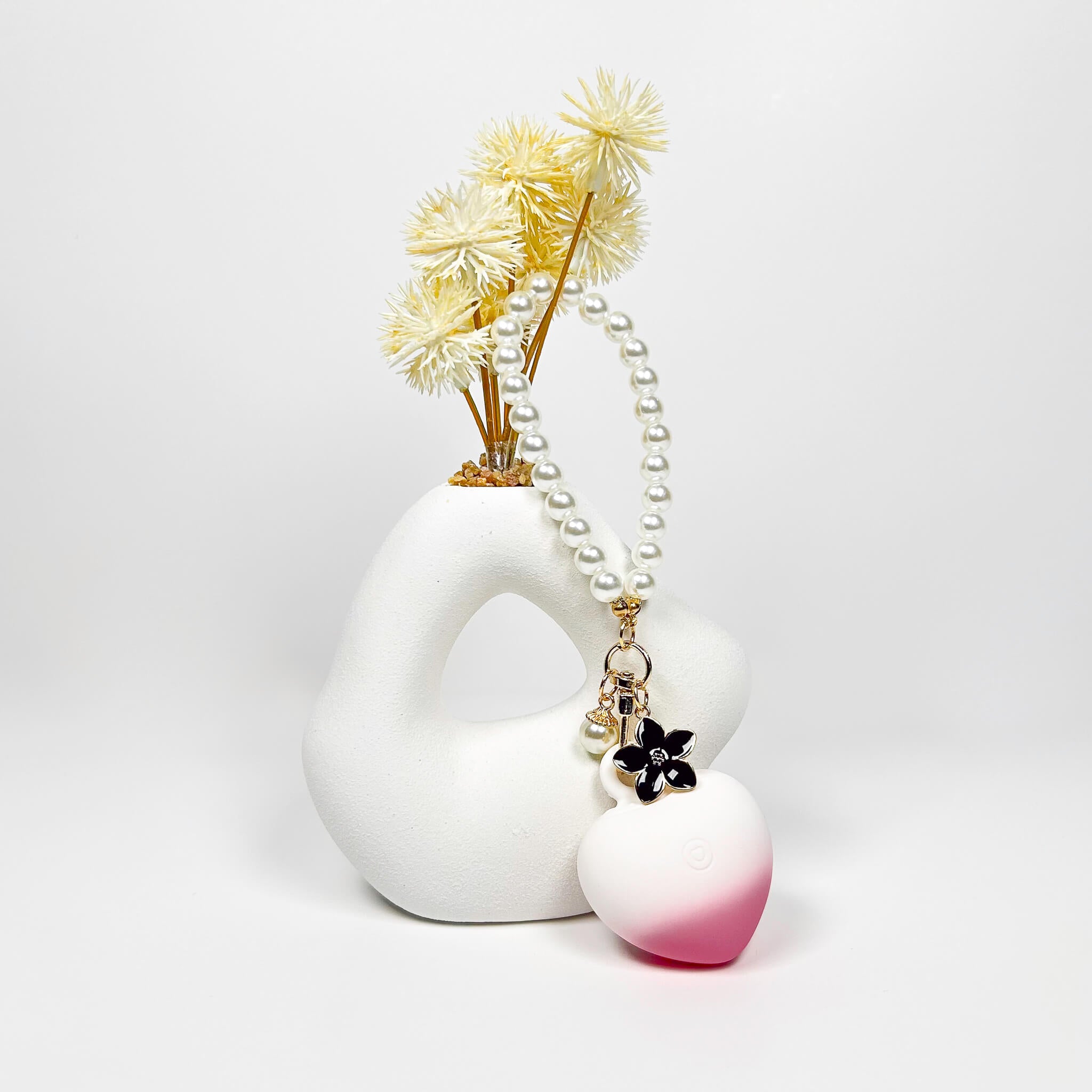 White ceramic vase with dried flowers and a HeartBeat Discreet Mini Vibrator on a light gray background