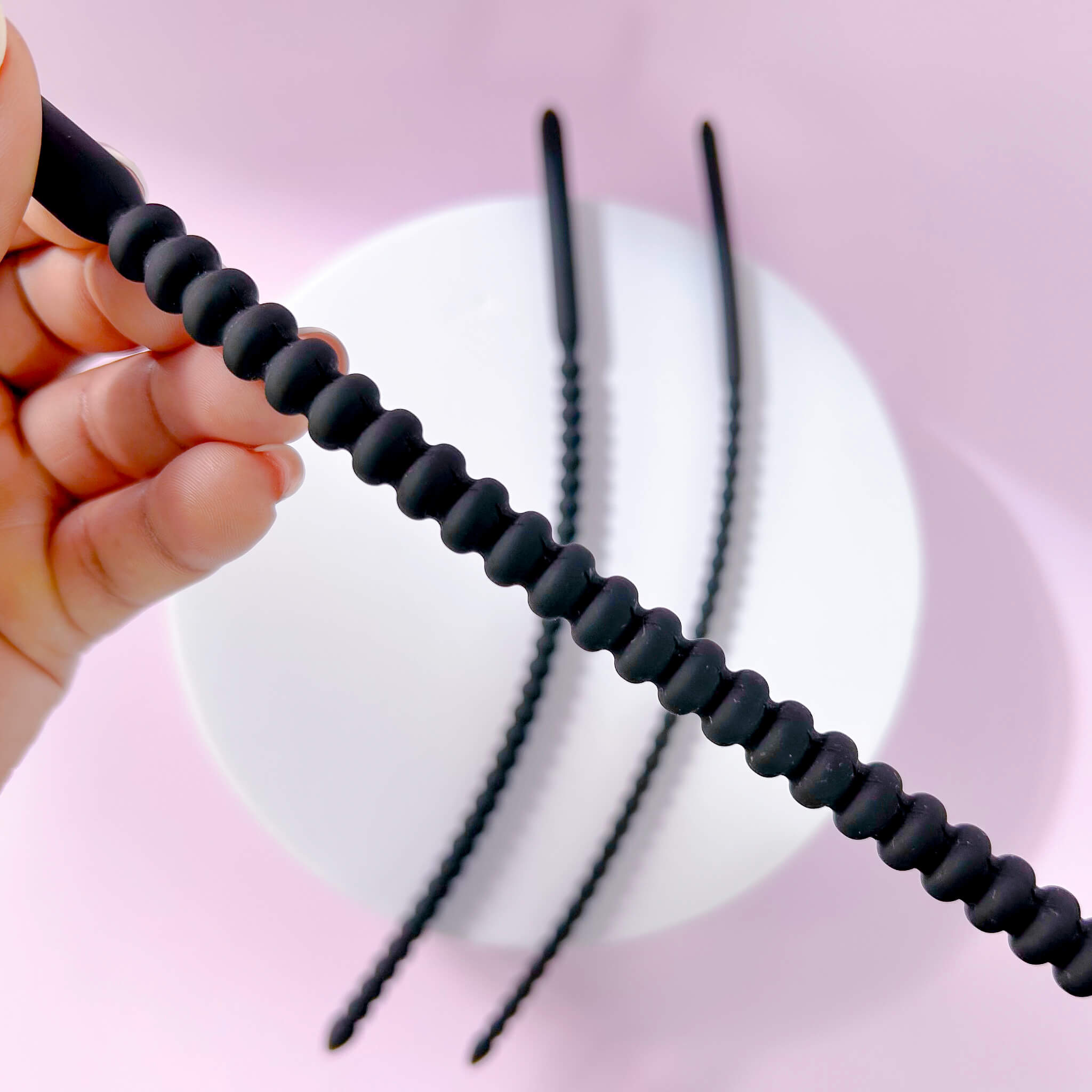 Large Ribbed Silicone Urethral Plug held by a hand against a pink background