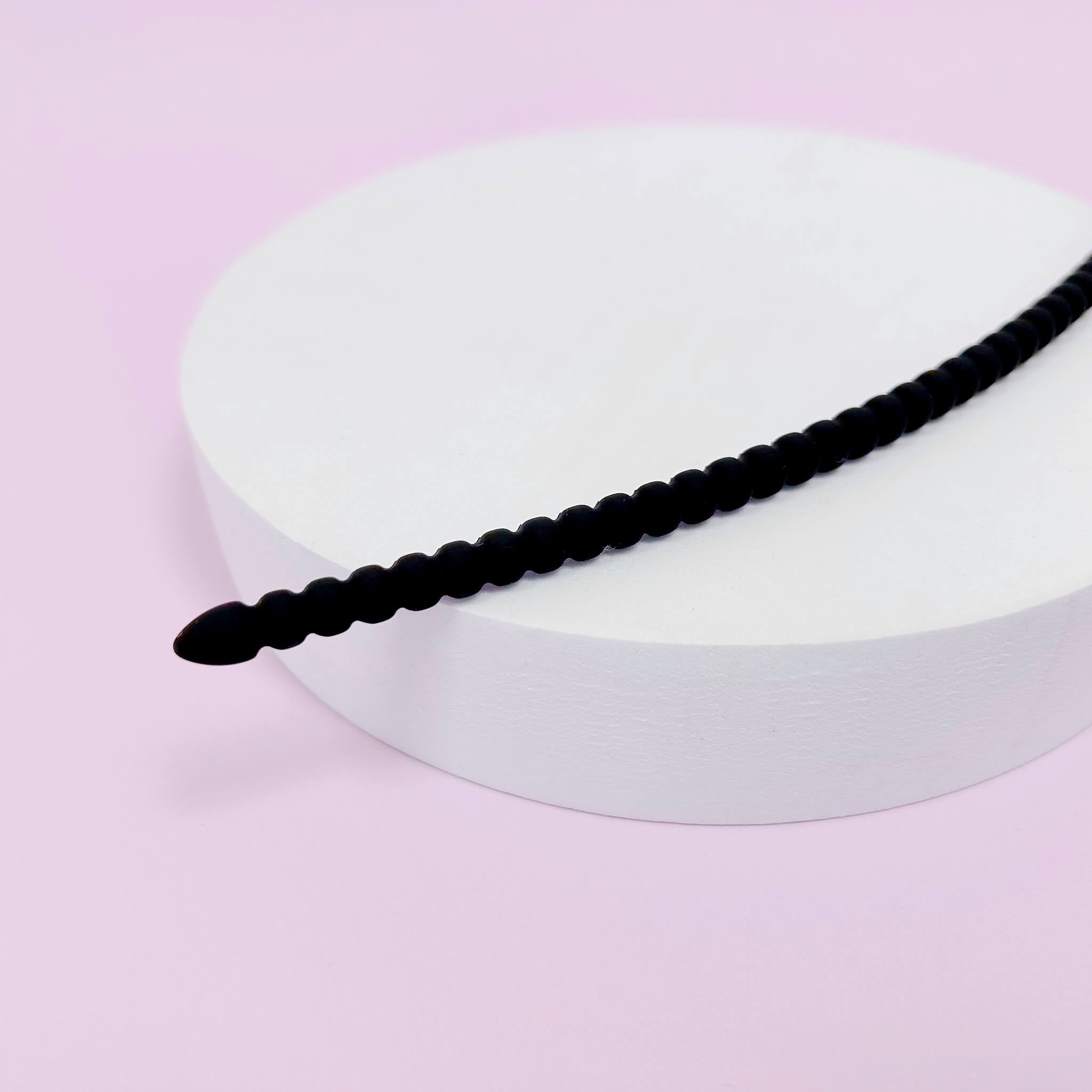 Medium ribbed Silicone Urethral Plug on a white circular stand against a pink background