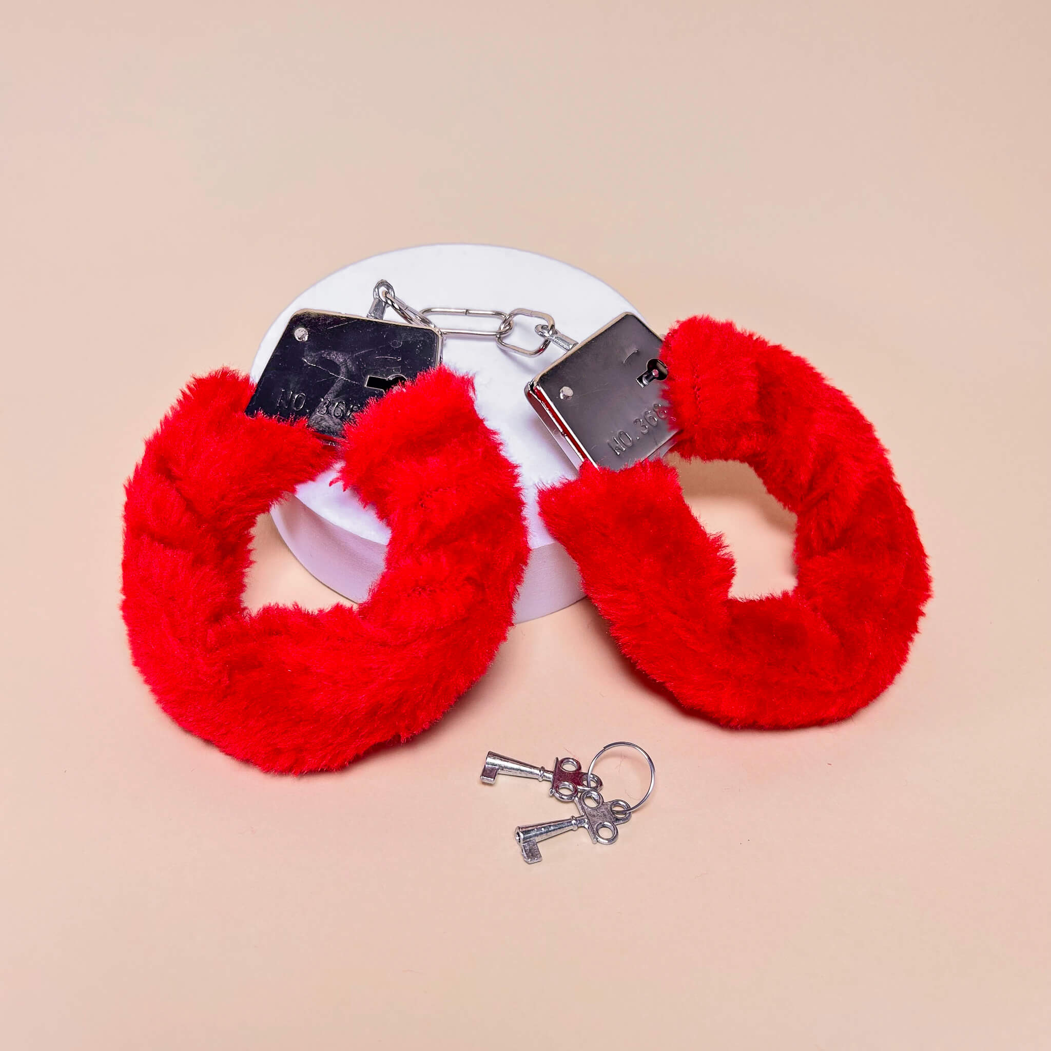 Red fluffy handcuffs with keys on a beige background