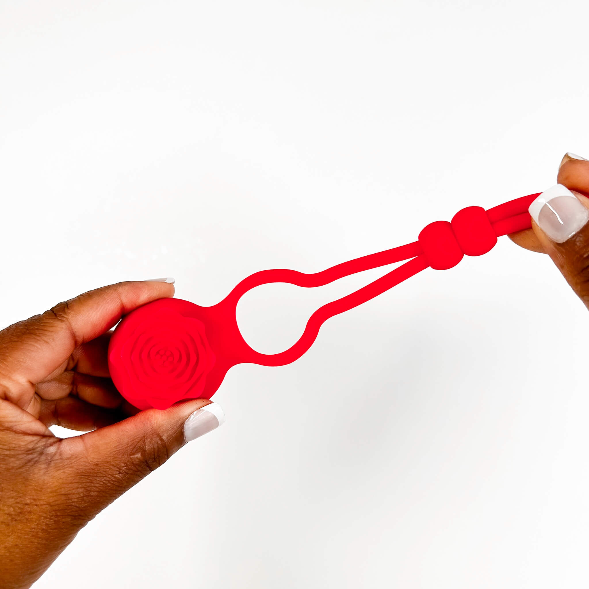 Red silicone adjustable vibrating cock rings held by two hands on a white background