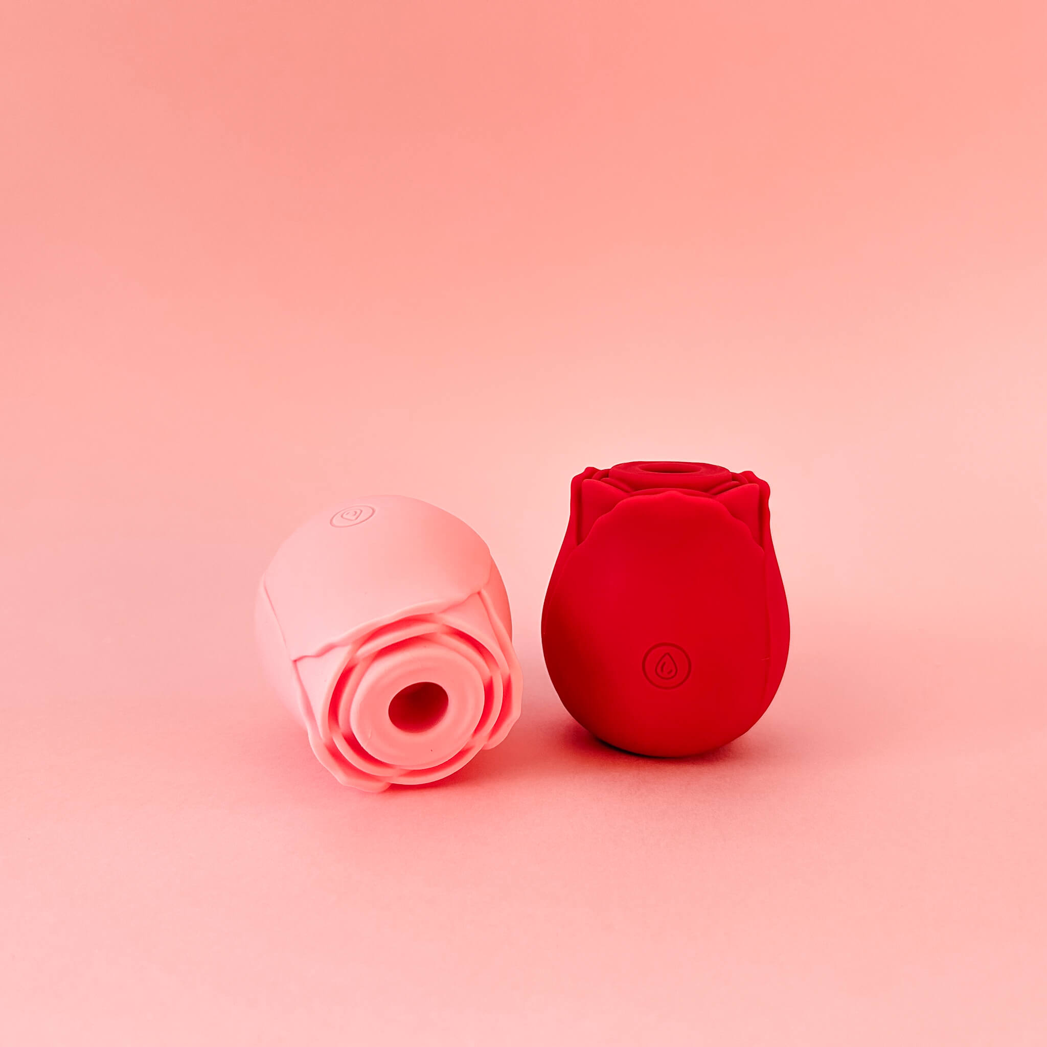 Two silicone rose-shaped products, one pink and one red, on a pink background.