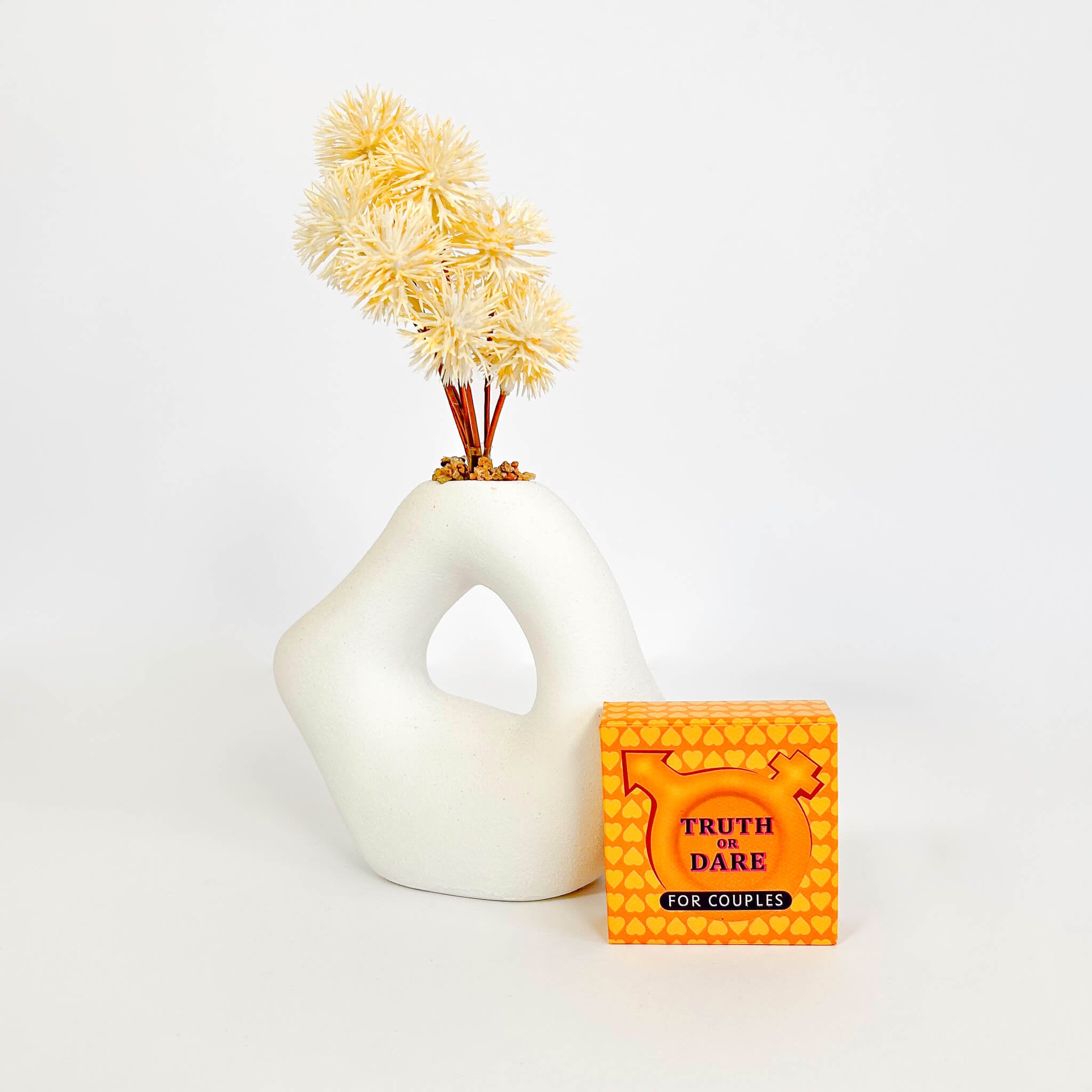 White vase with dried flowers and a 'Truth Dare for Couples' box on a white background