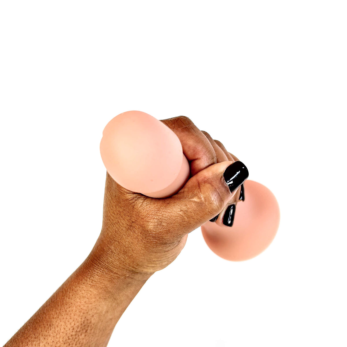 A hand with black nail polish squeezes a peach-colored silicone stress ball against a solid white background.