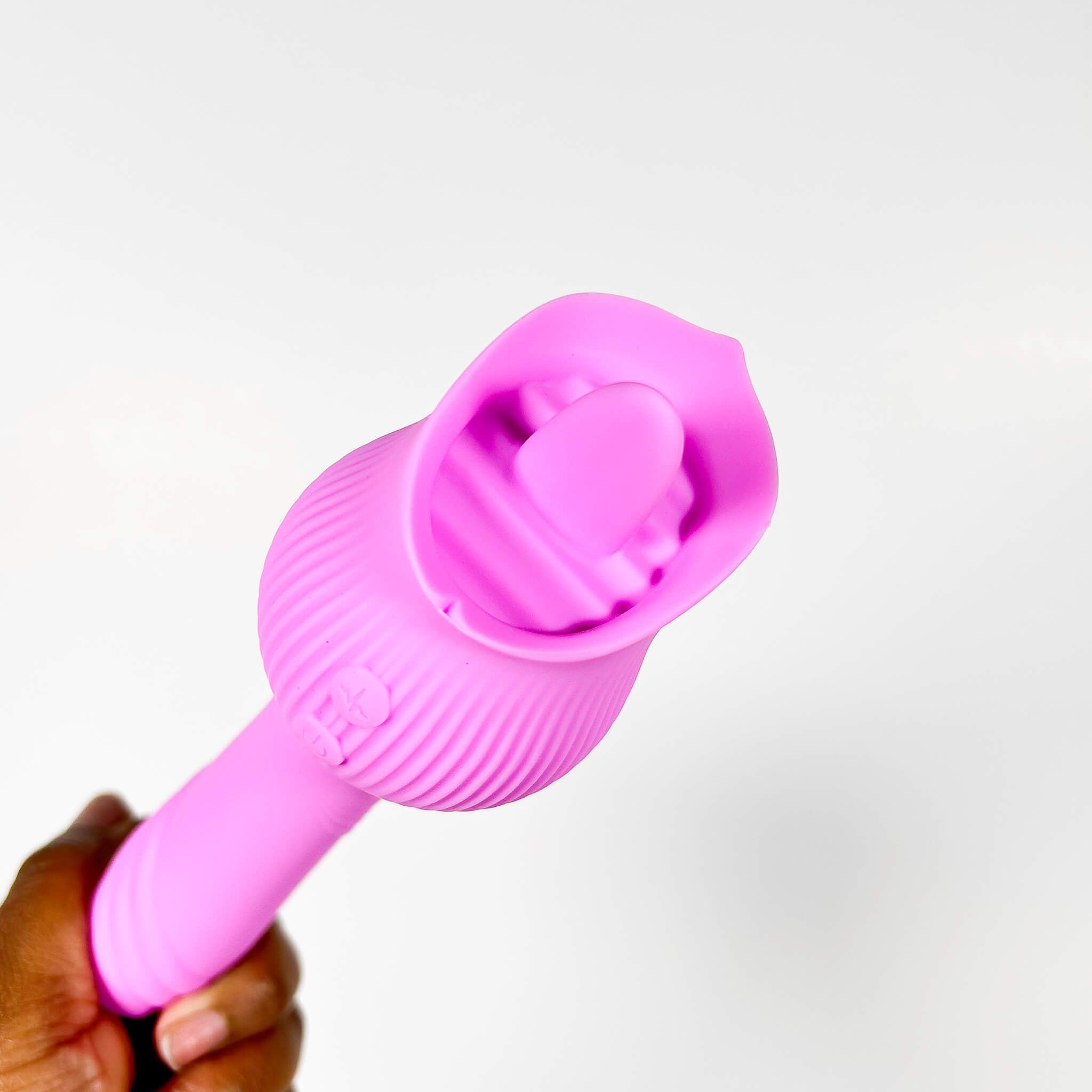 Pink silicone dual tongue vibrator held by a hand on a white background