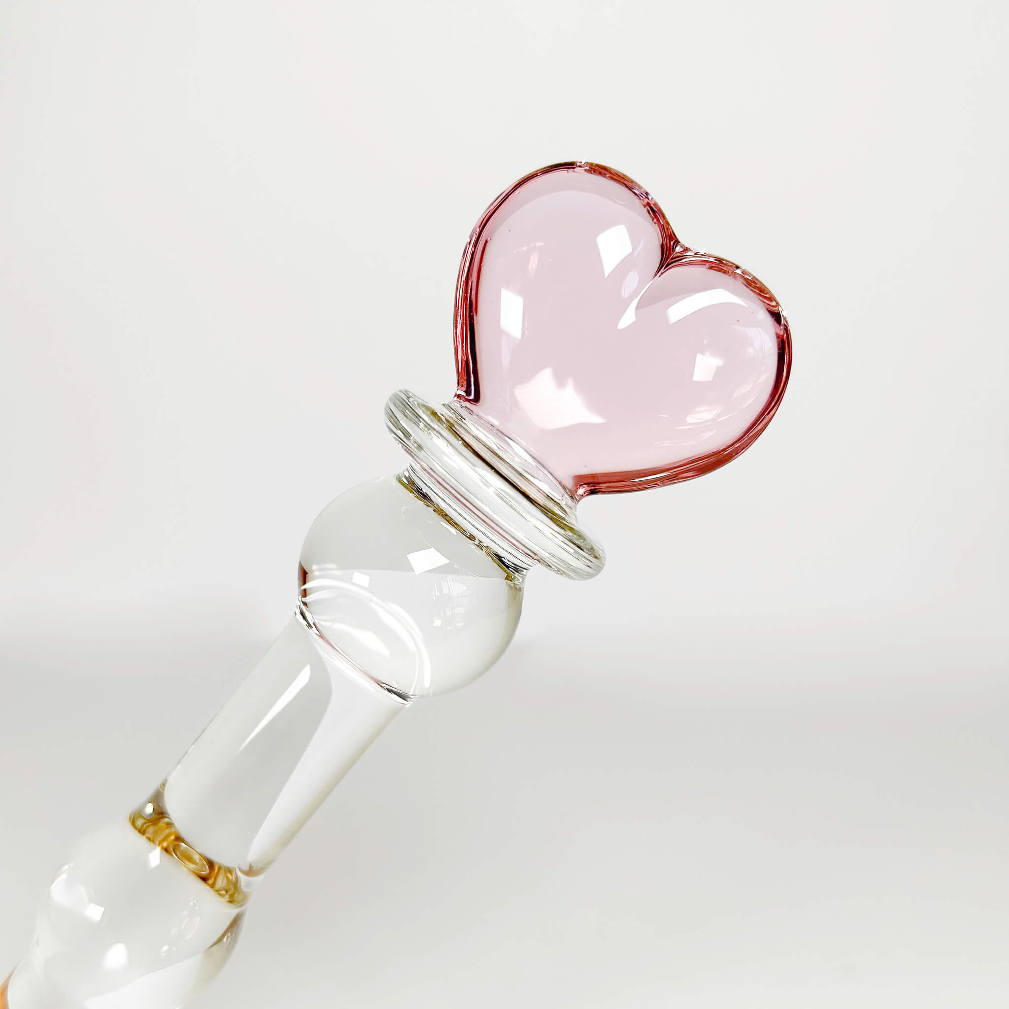 Glass dildo with a pink heart-shaped stopper on a white background