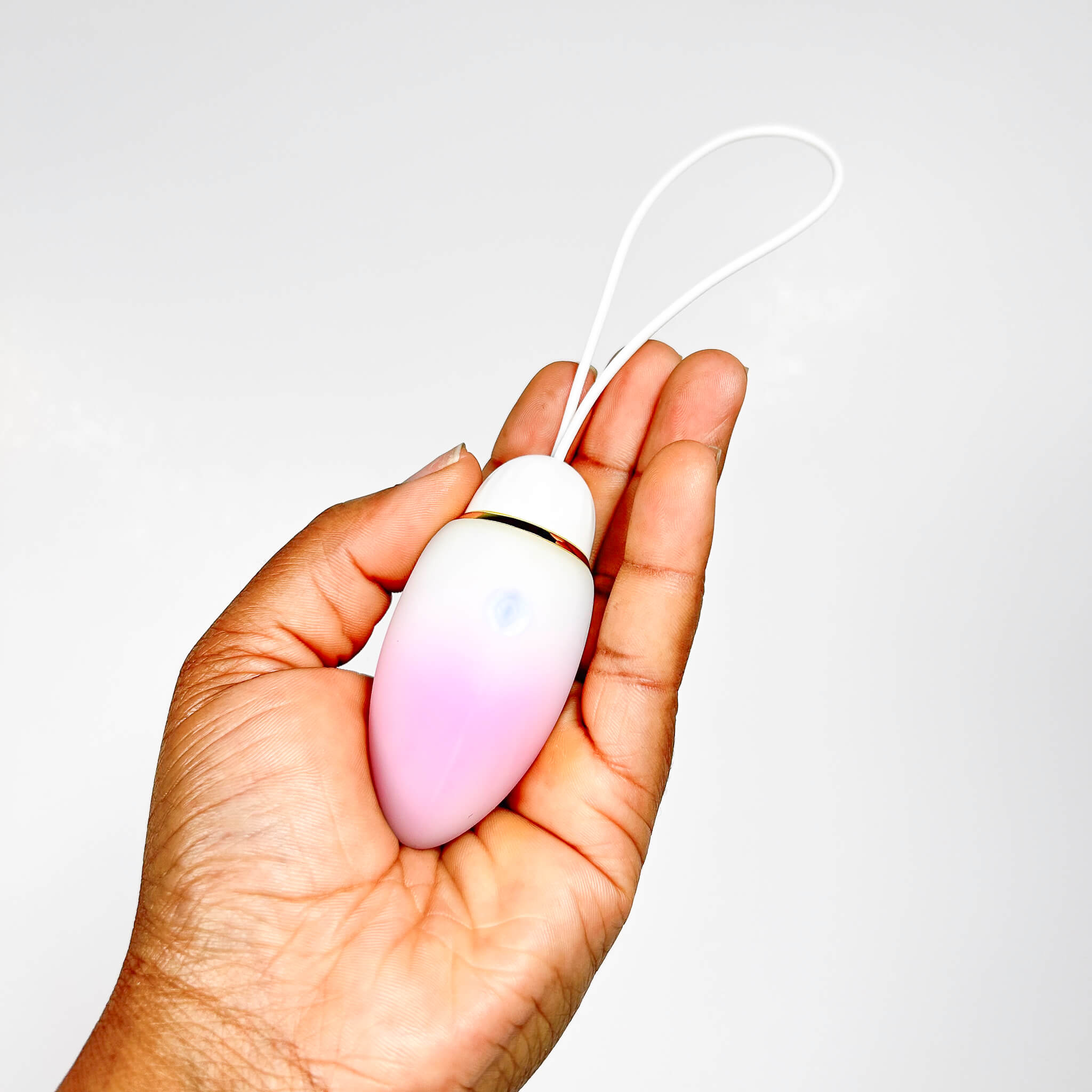 Hand holding a pink and white egg-shaped jumping egg sex toy with a string on a light gray background