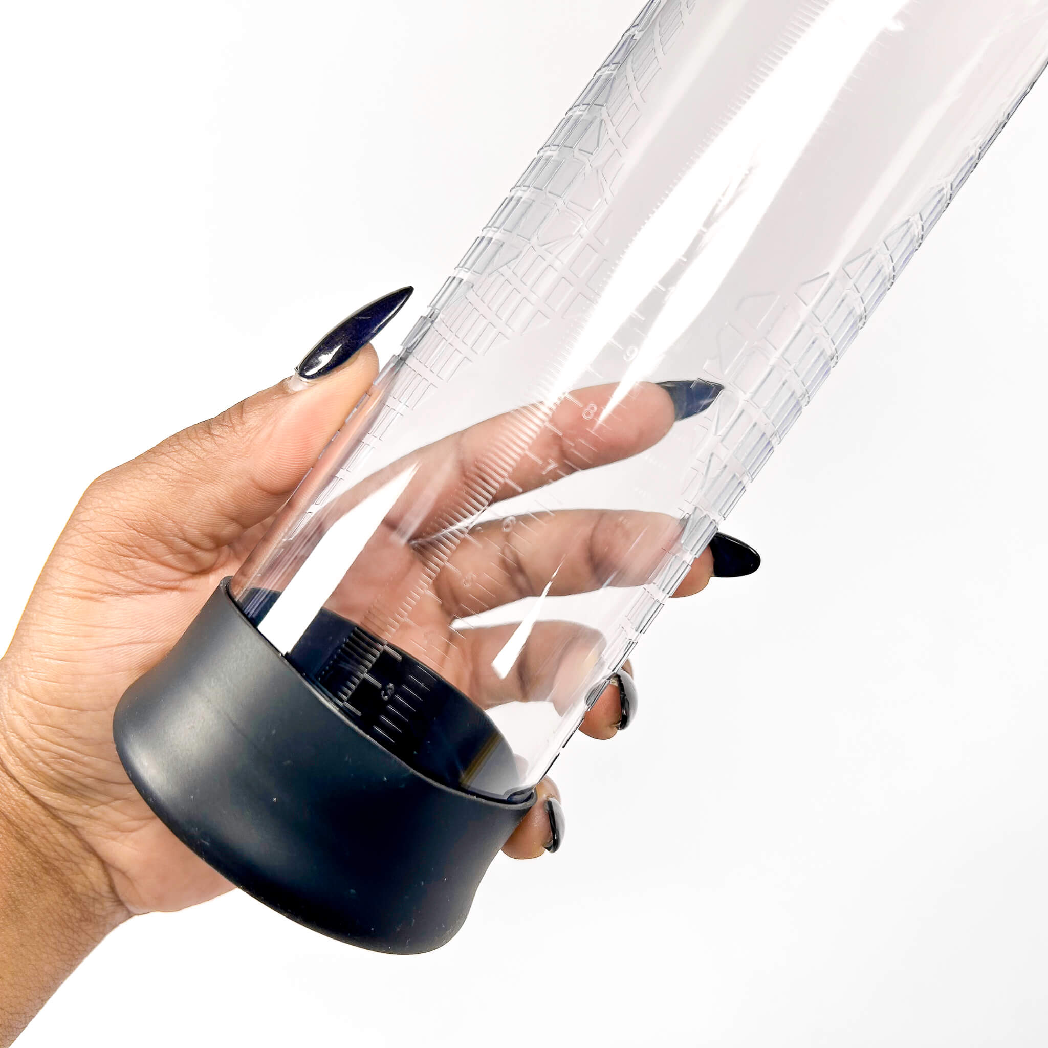 Hand holding a transparent acrylic penis pump clyinder with black base on a white background
