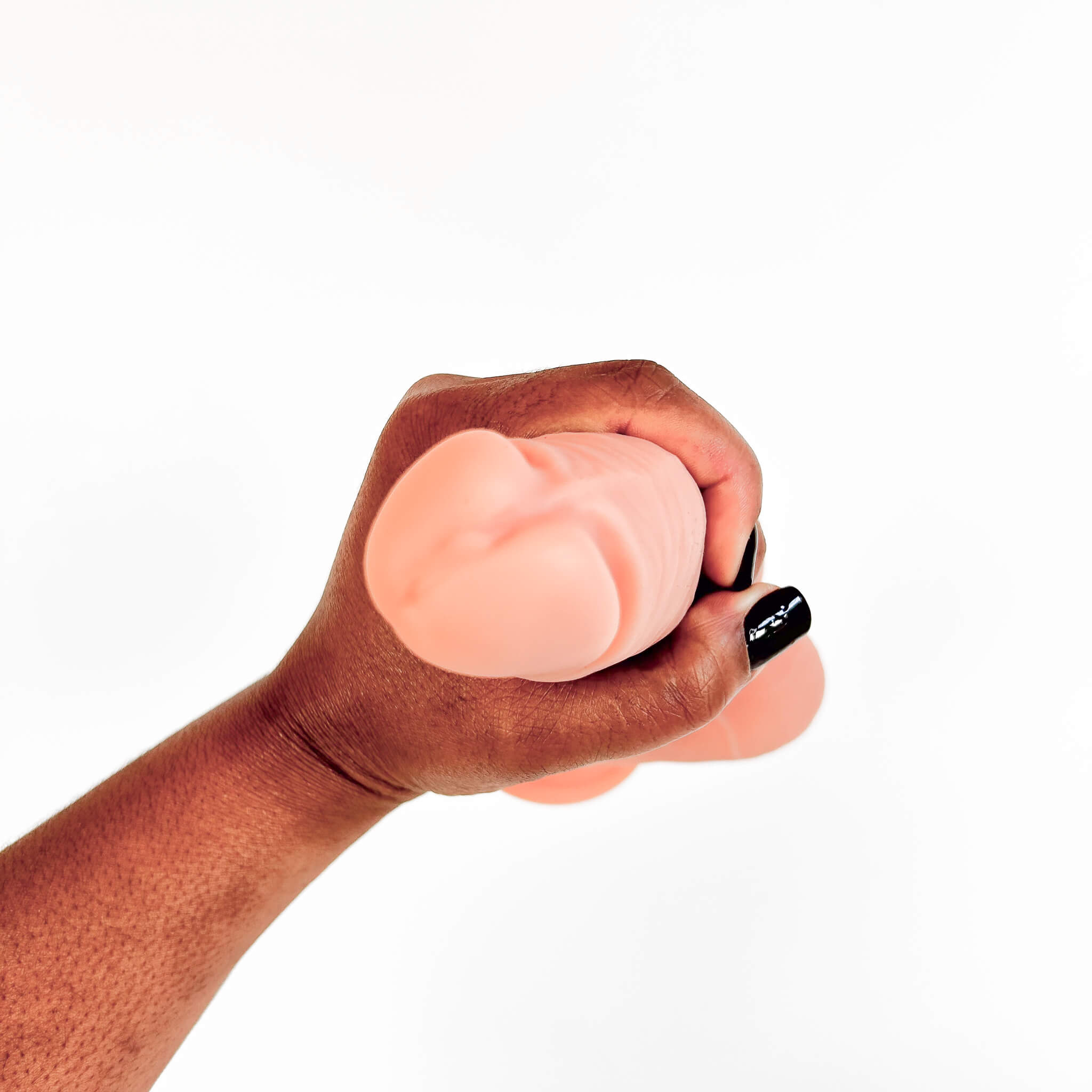 A hand with black nail polish holds a flesh-toned silicone adult novelty item against a plain white background.