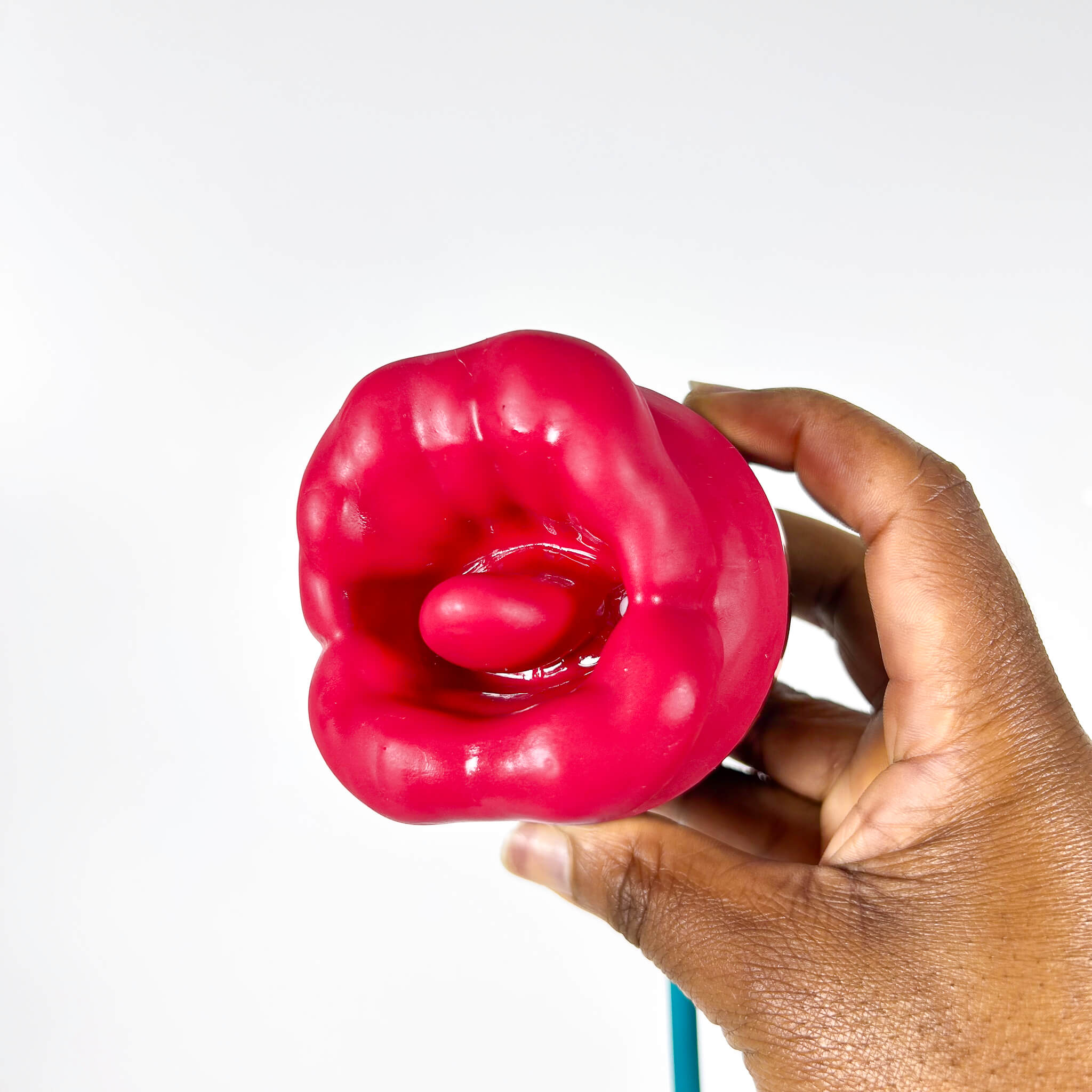 Hand holding a bright pink red tongue vibrator against a white background