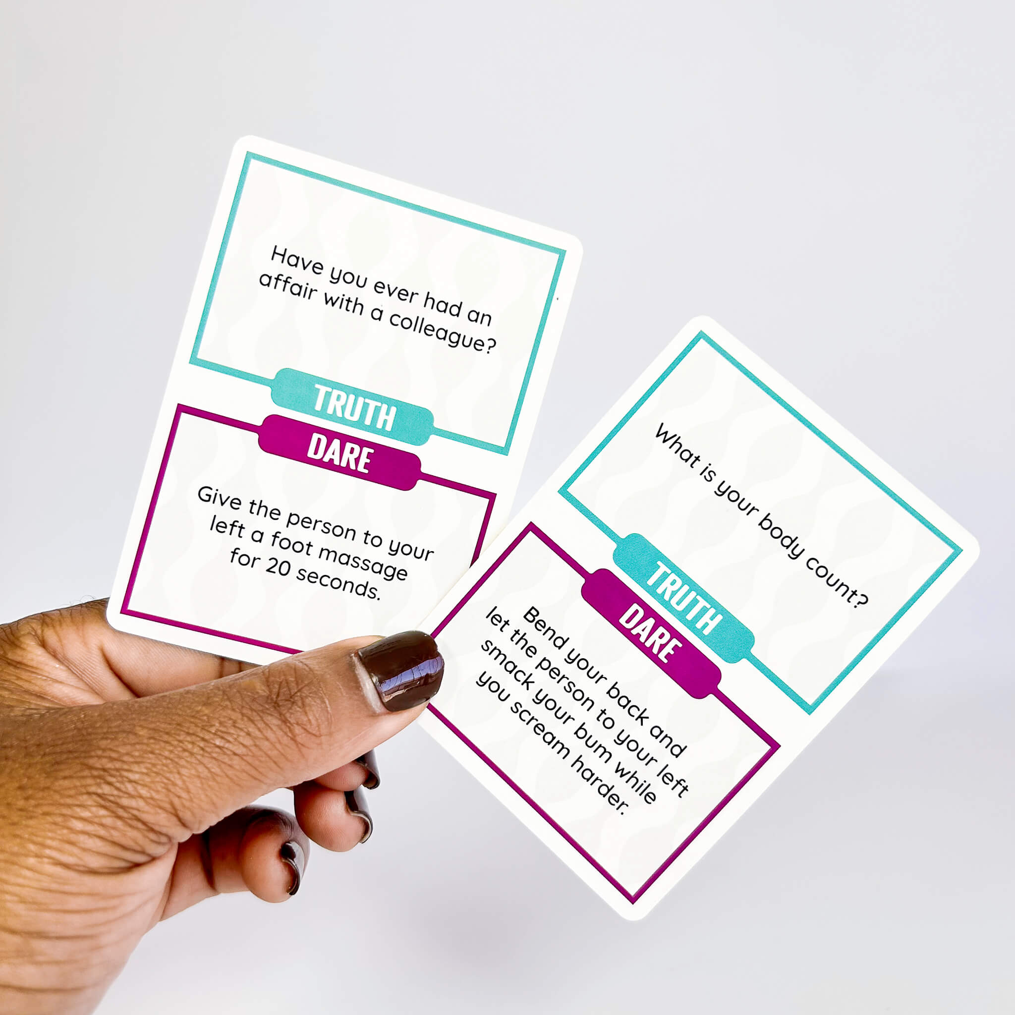 Hand holding two truth or dare cards with text on a light gray background