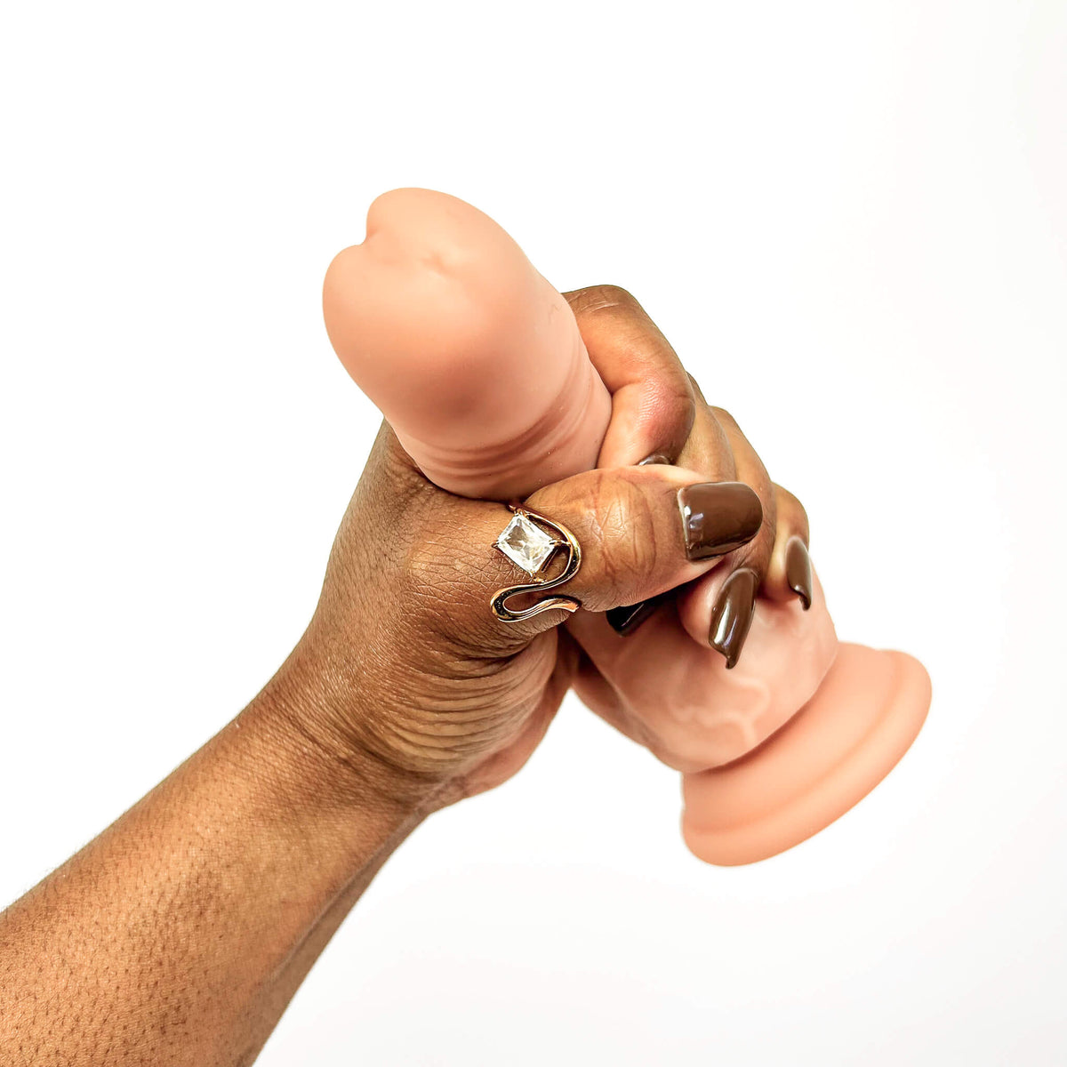 A close-up of a hand holding a realistic flesh-toned dildo against a plain white background.