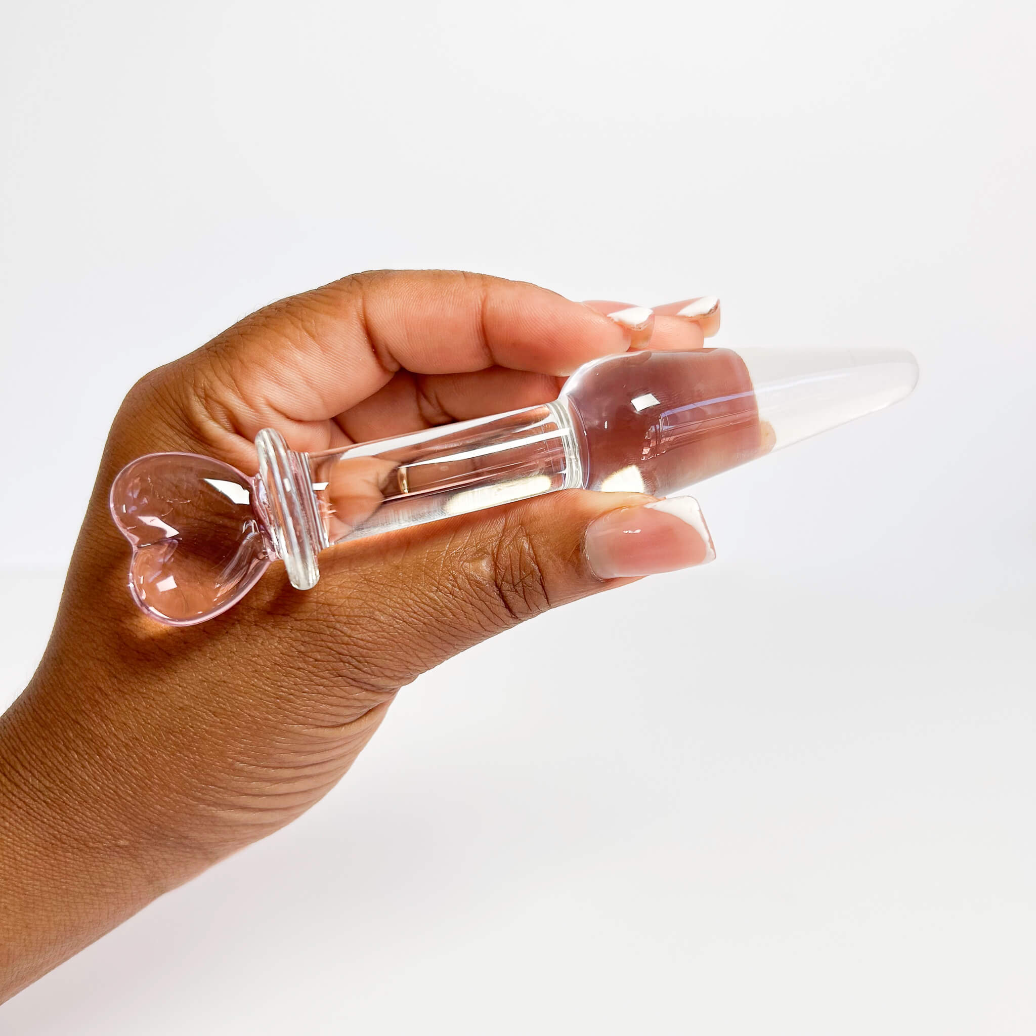 Hand holding a small glass butt plug with heart-shaped ends on a white background