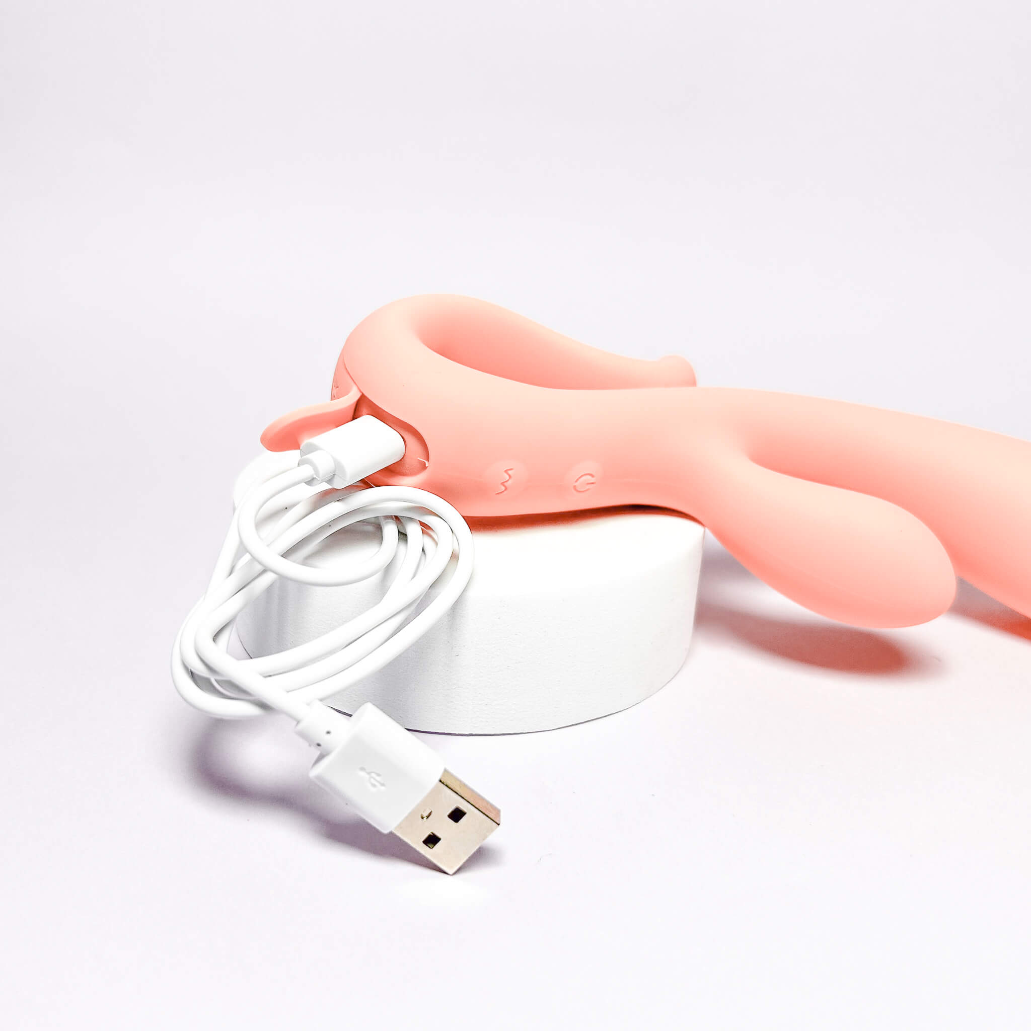 Pink handheld vibrator with a white USB cable on a light gray background