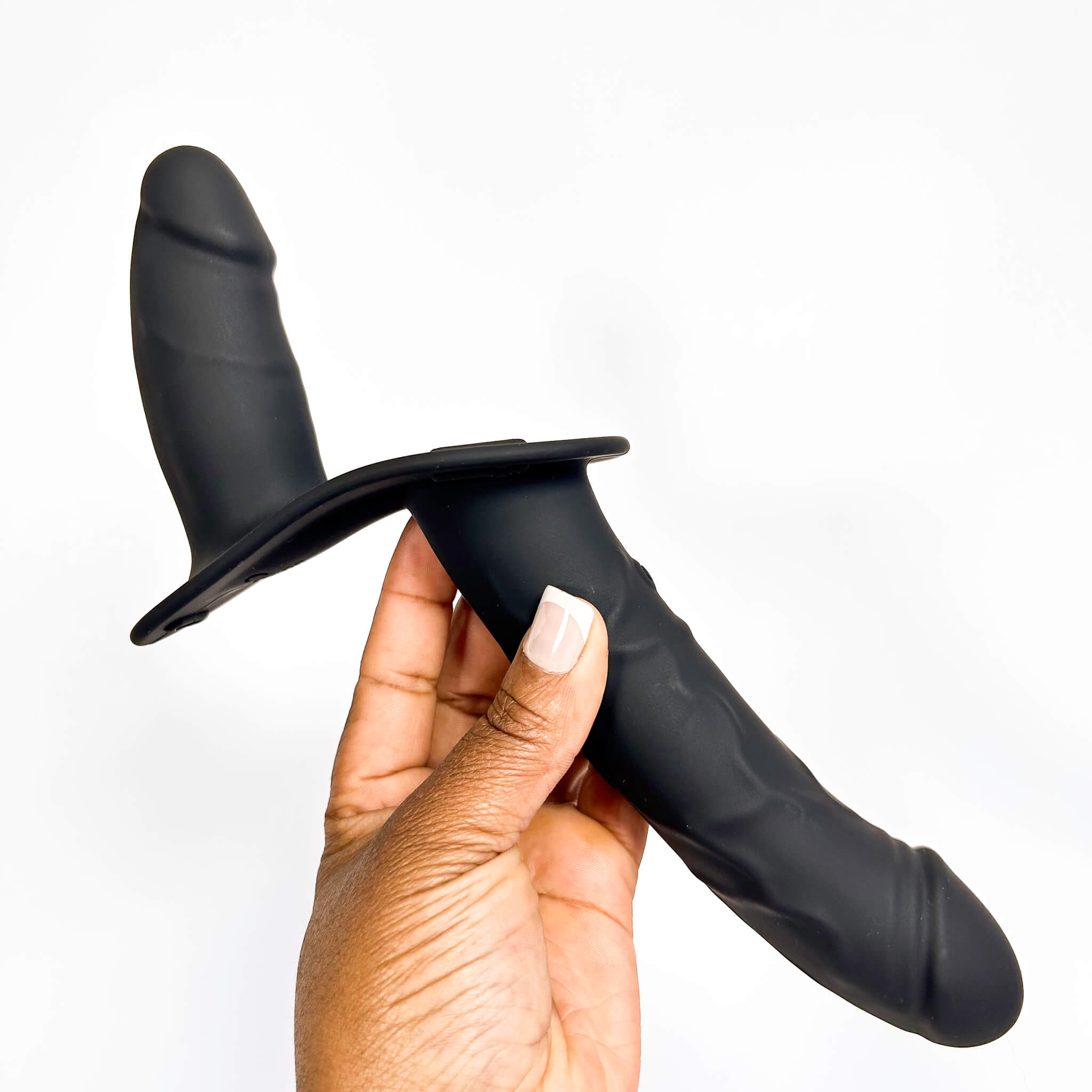 A hand holding a black silicone dual-stimulation dildo against a plain white background.