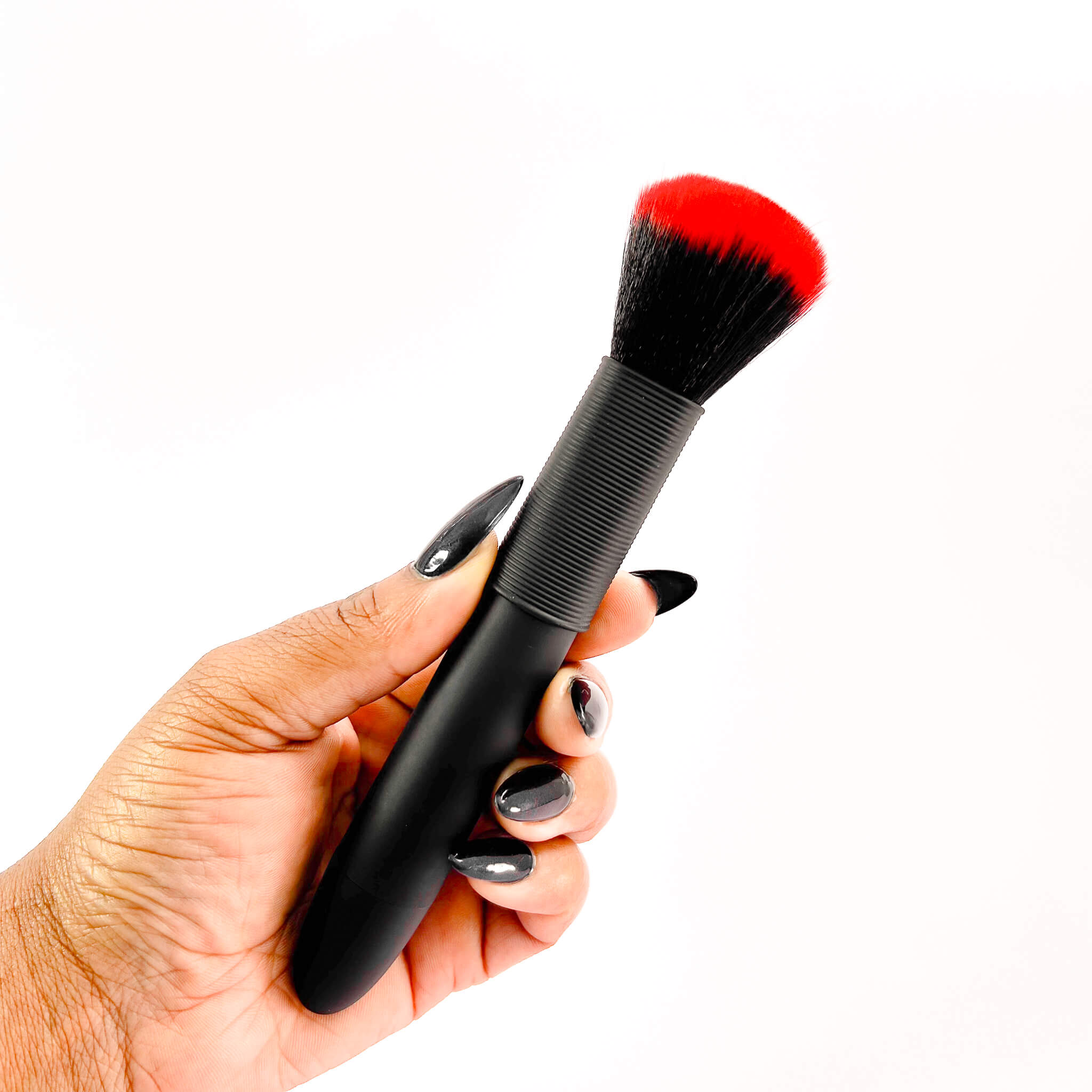 Hand holding a black vibrator makeup brush with red bristle tip on a white background