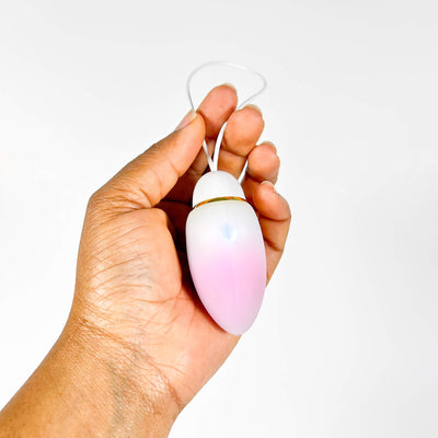 Hand holding a pink and white egg-shaped vibrator against a white background
