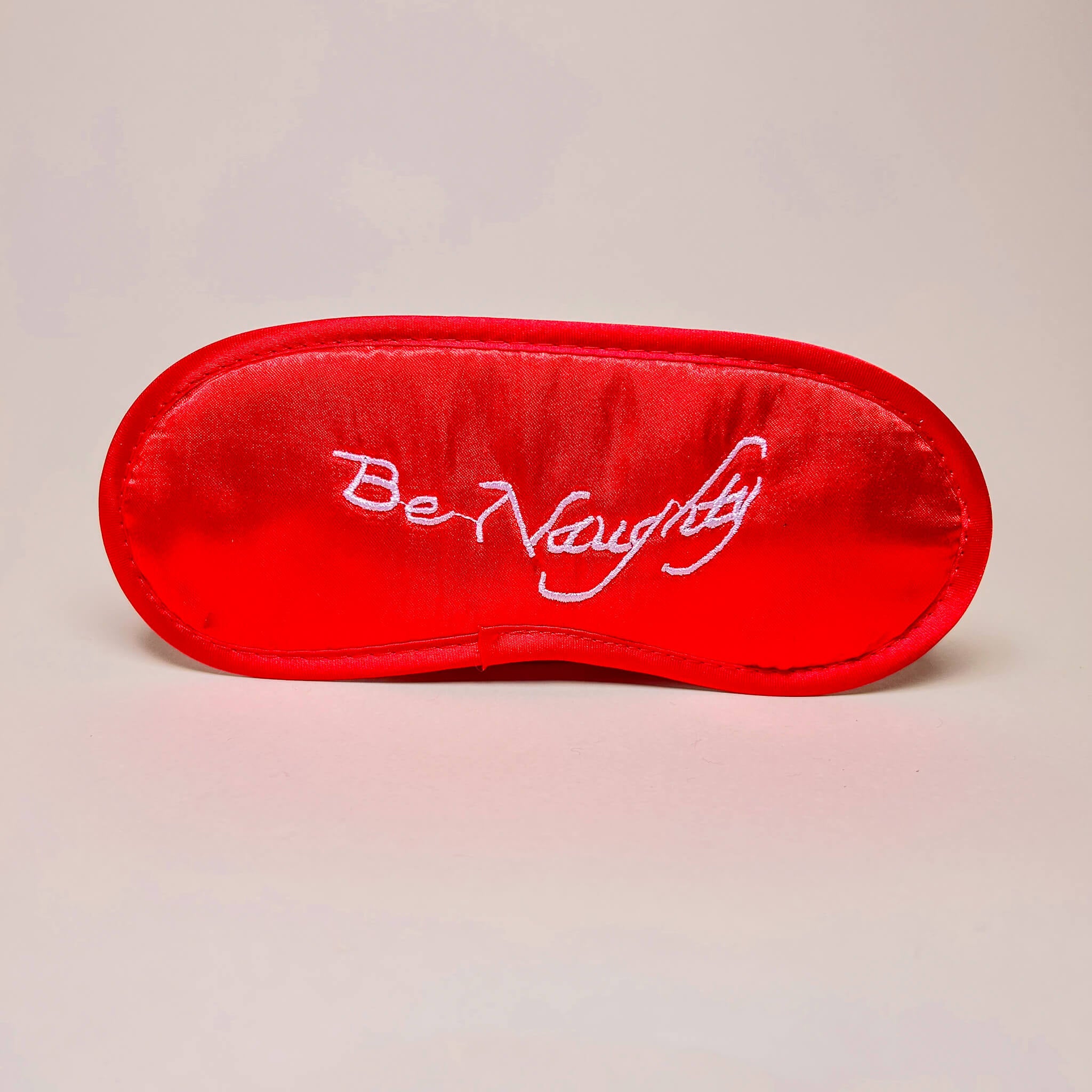 Red bedroom mask with 'Be Naughty' text on a beige background