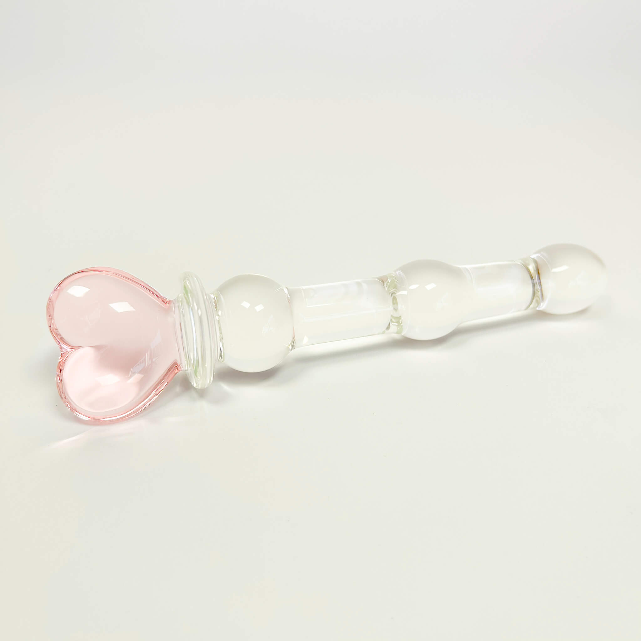Beaded Glass Dildo with a pink heart-shaped piece on a light gray background