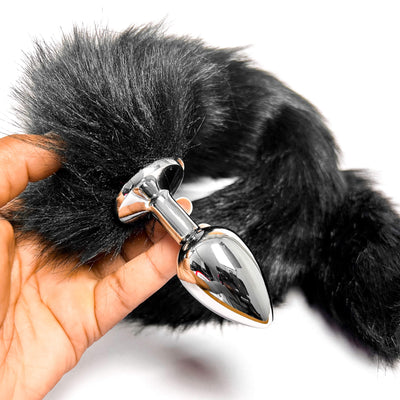 Black Extra Long Tail With Metal Butt Plug held by a hand on a white background