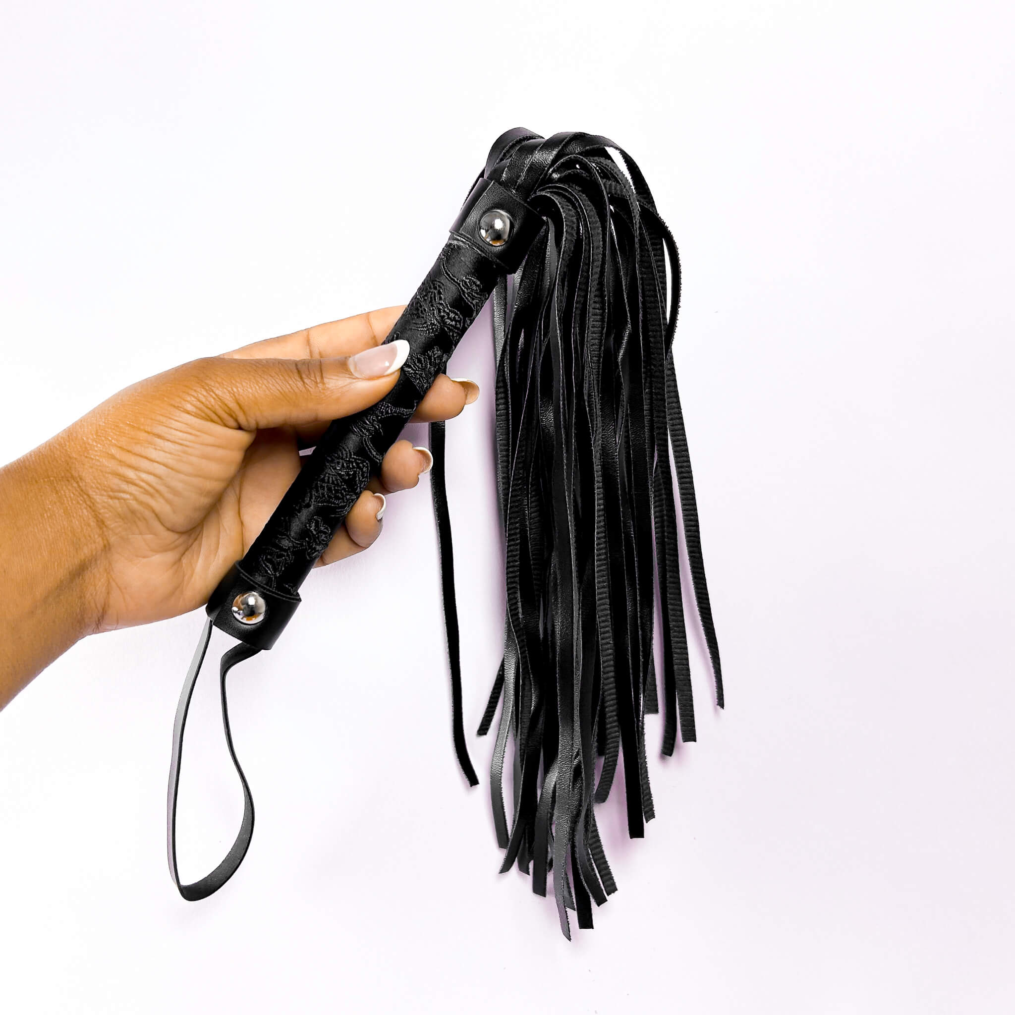 Black leather flogger held by a hand on a white background