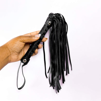 Black leather flogger held by a hand on a white background