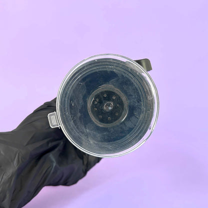 Clear plastic component held by a black gloved hand against a purple background