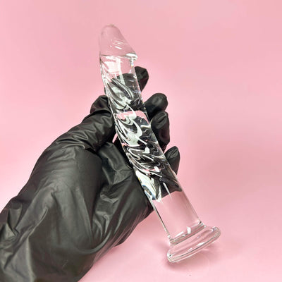 Veiny Glass dildo held by a gloved hand against a pink background