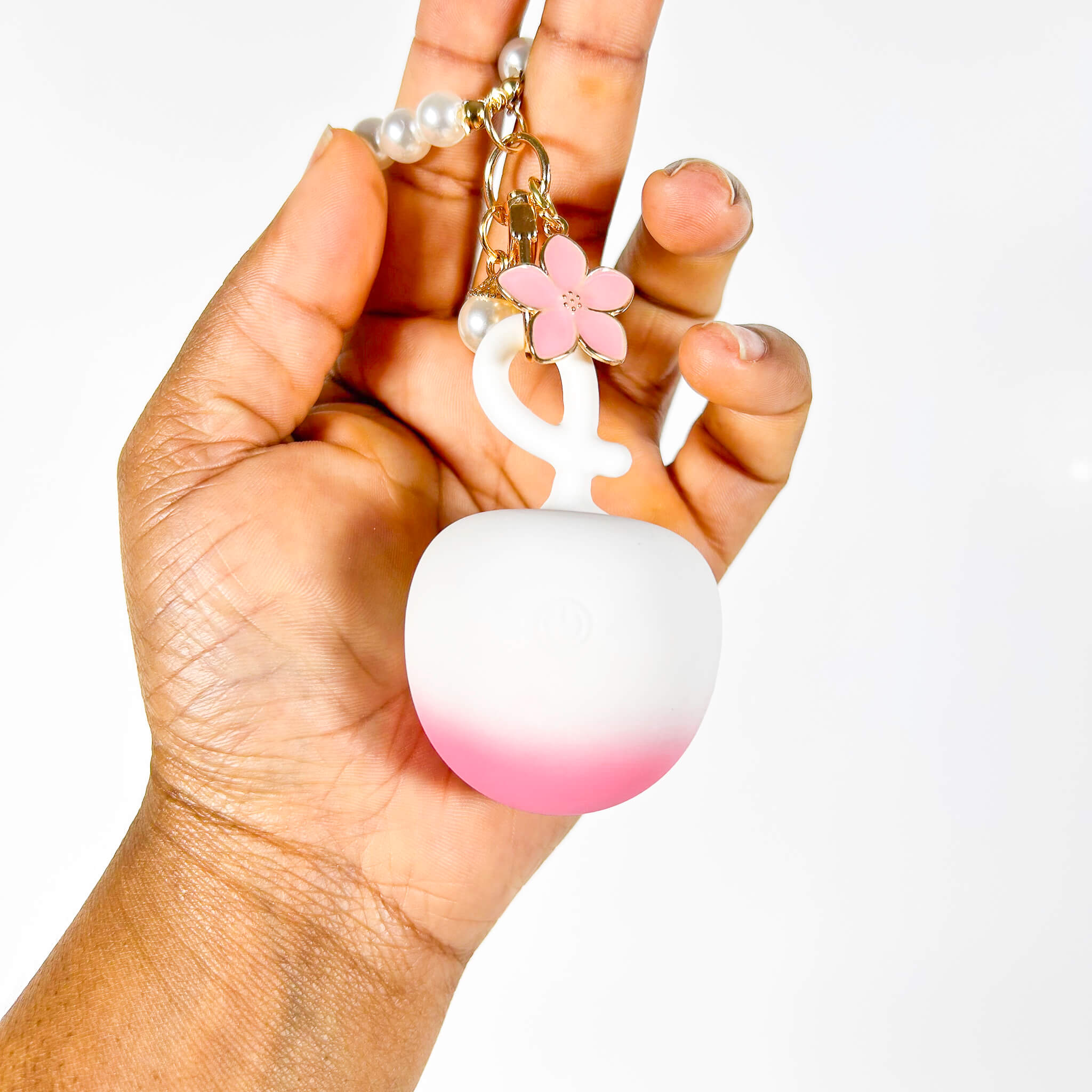 Hand holding a pink and white gradient Discreet Mini Vibrator with a flower charm against a white background