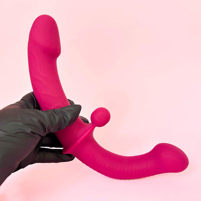 Double Ended Dildo Vibrator With Clit Stimulator Ball held by a gloved hand against a pink background