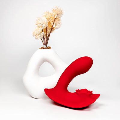 White vase with dried flowers and a red Double Tease Insertable App Controlled Panty Vibrator on a white background