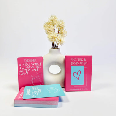 Excited & Exhausted Couples drinking game cards with a decorative vase on a white background