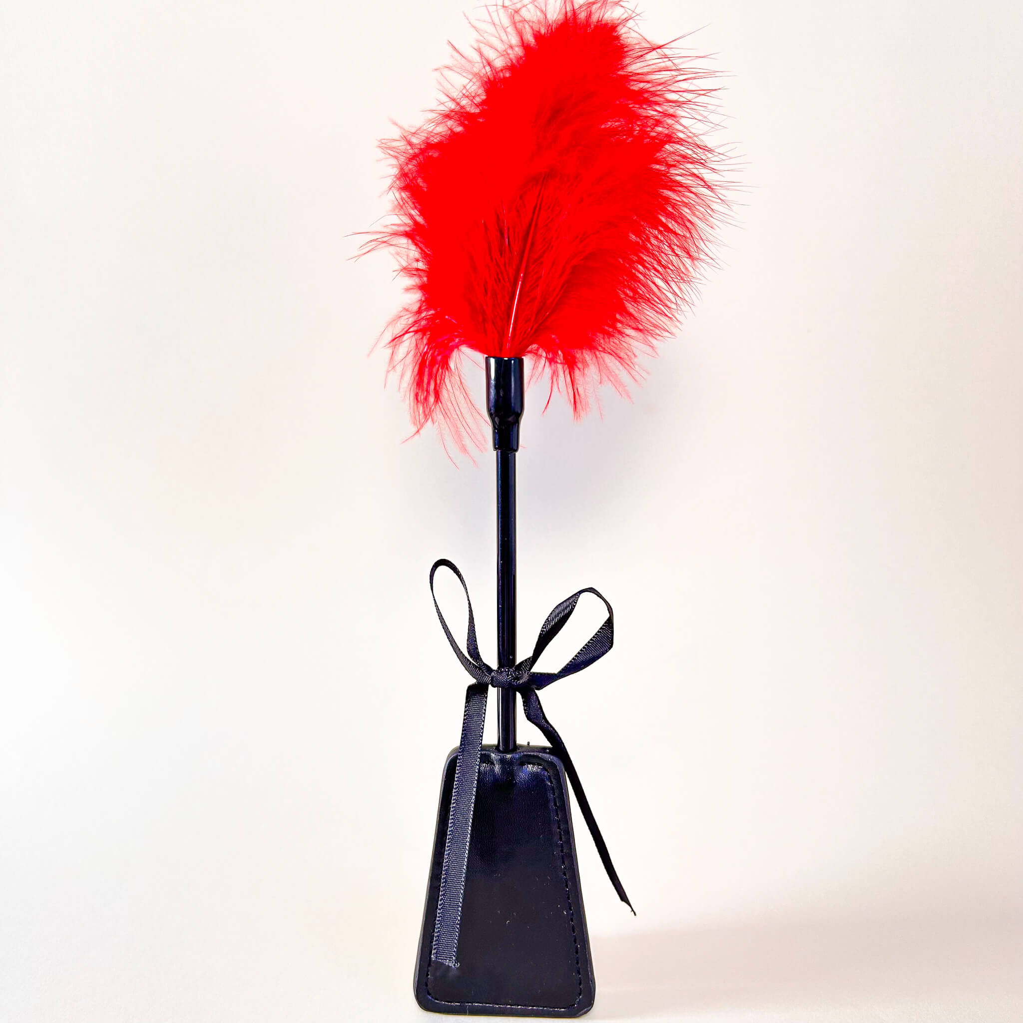 Black leather paddle with red feather on a white background