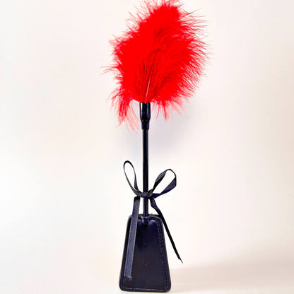 Black leather paddle with red feather on a white background