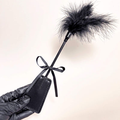 Black leather paddle with feathered end held by a gloved hand on a light background