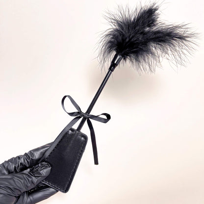Black leather paddle with feathered end held by a gloved hand on a light background