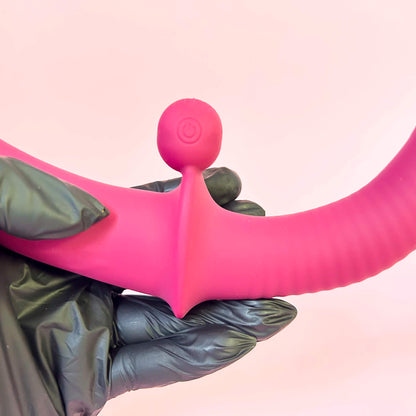 Flexible double ended vibrator held by a gloved hand against a pink background