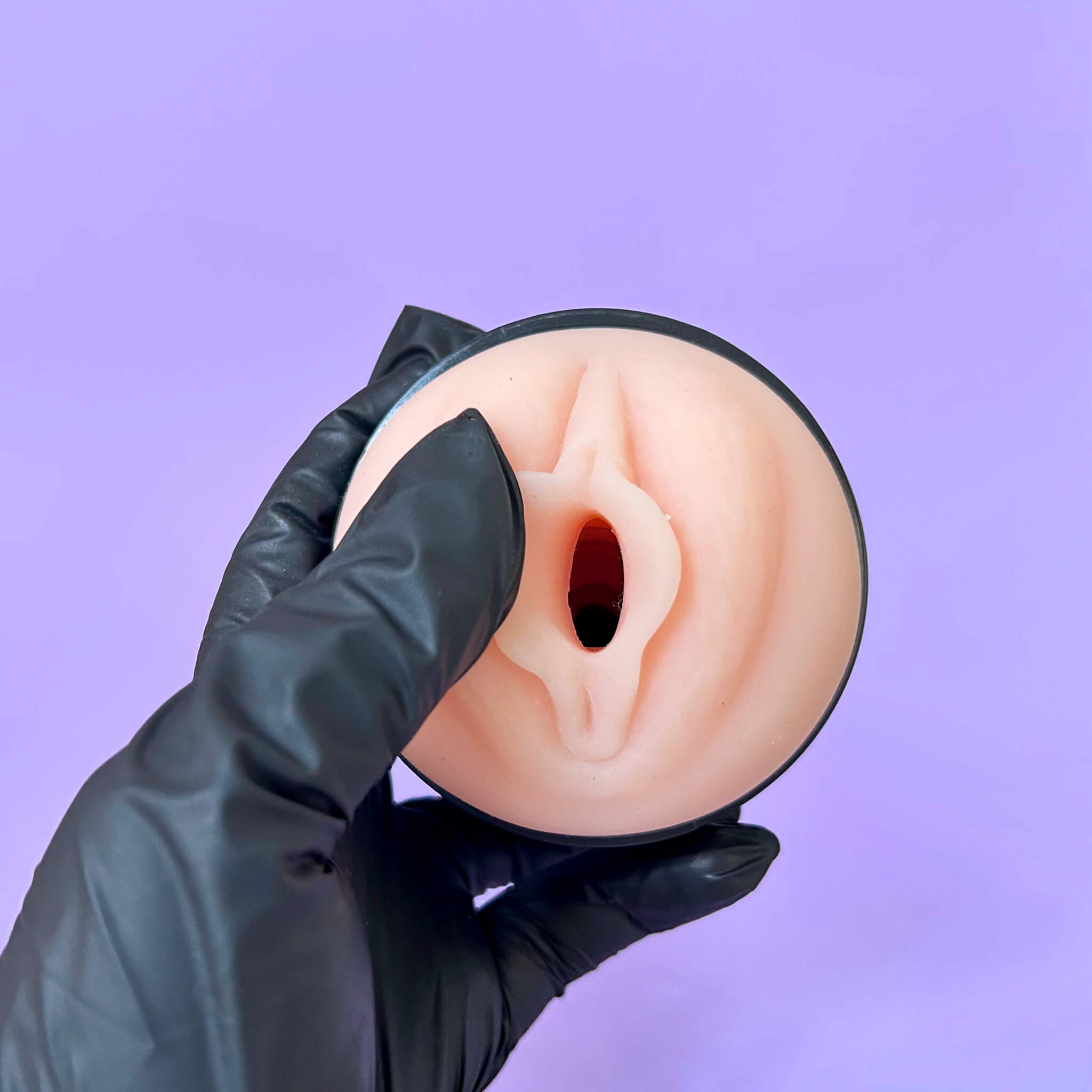 Handsfree Suction Cup Male Masturbator vagina held by a gloved hand against a purple background