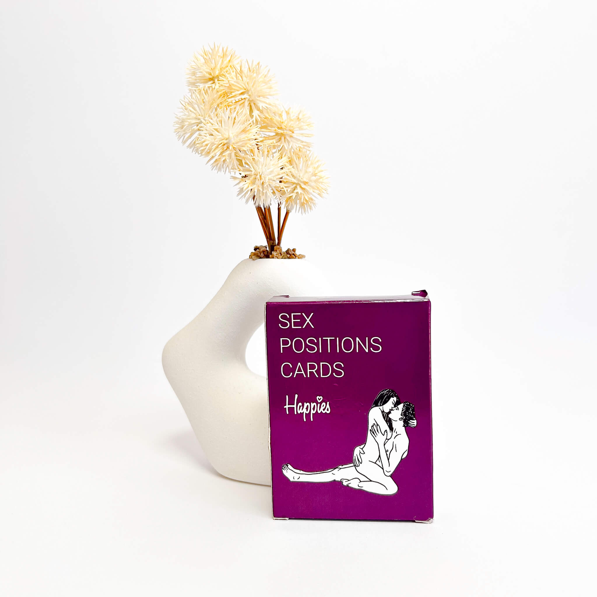 Purple card box labeled 'Sex Positions Cards' with a white vase and decorative plant on a white background